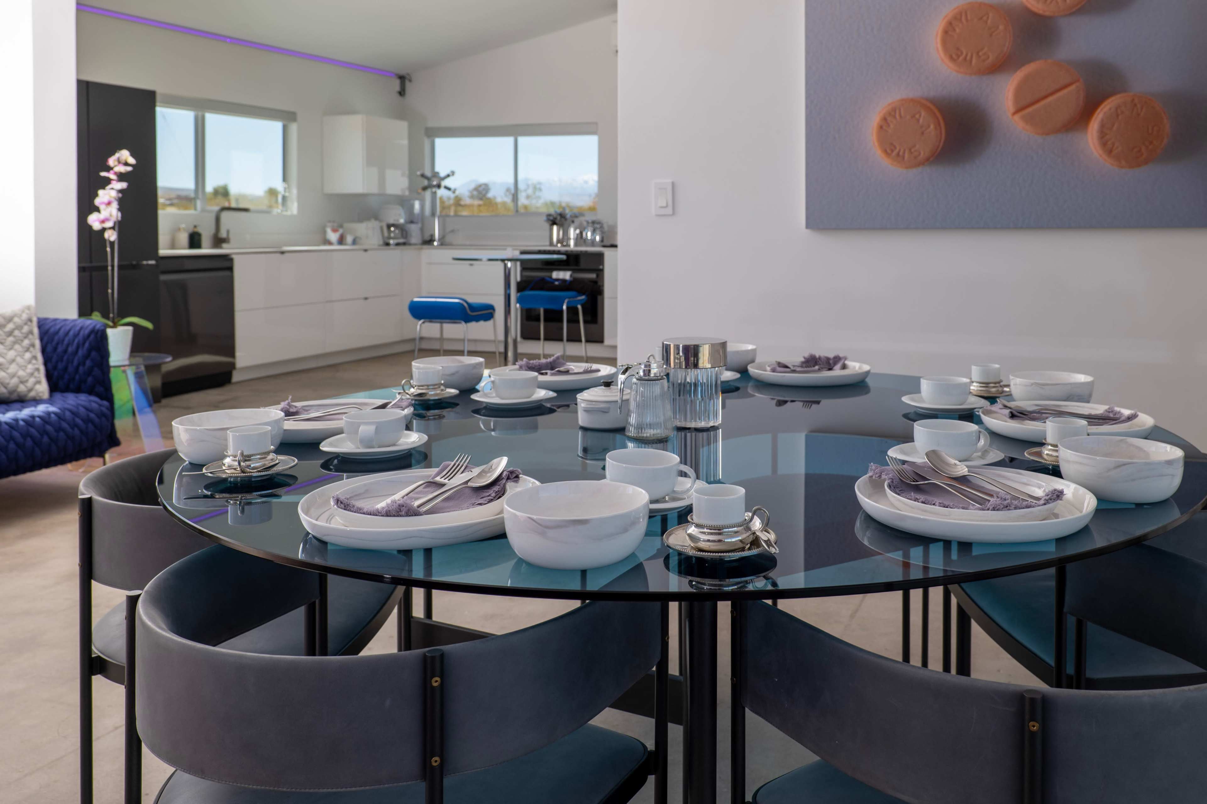 A round dining table is set with dishes and silverware in a modern kitchen and dining area.