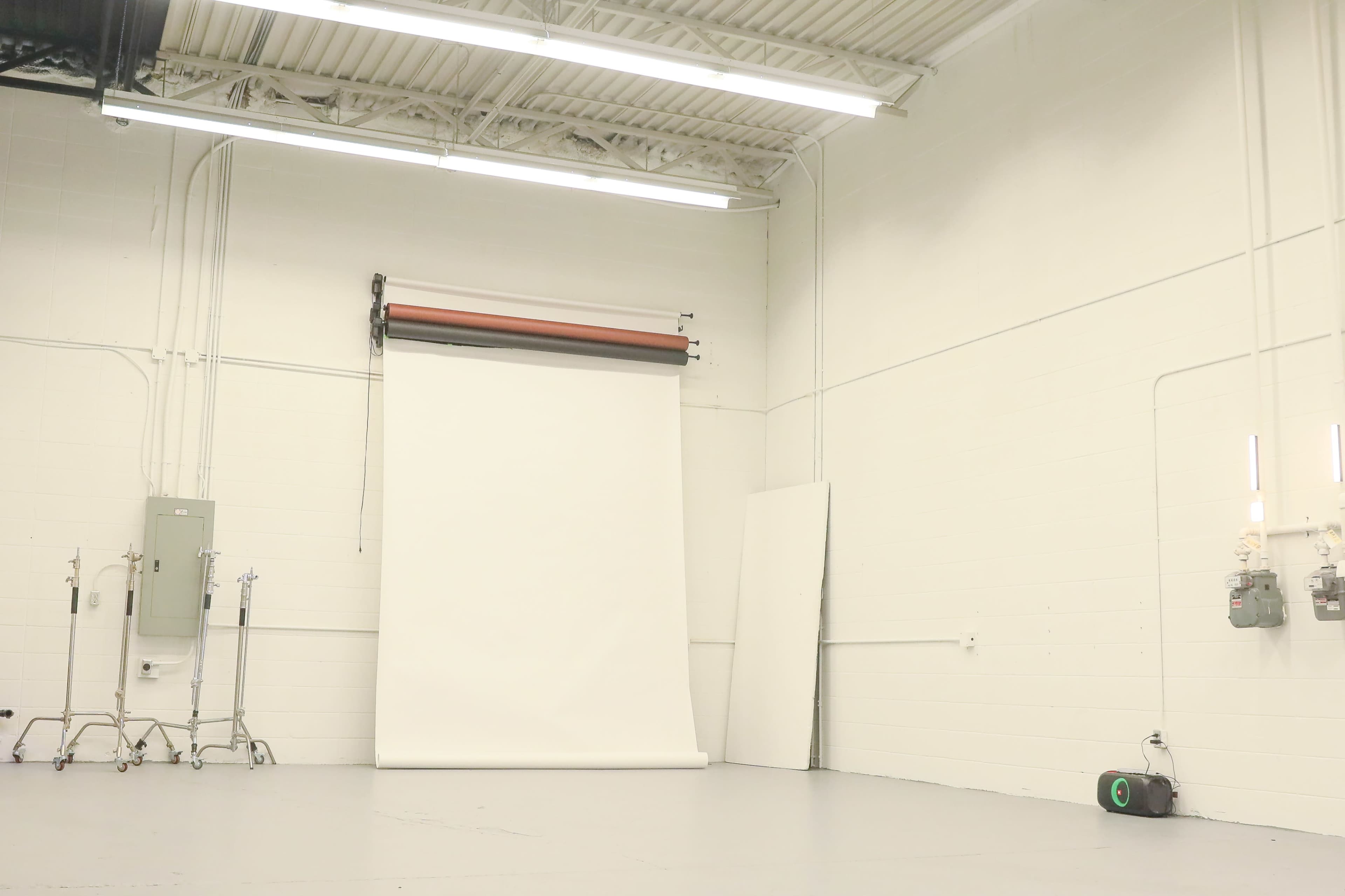 A large, empty photography studio with a white backdrop and industrial lighting.