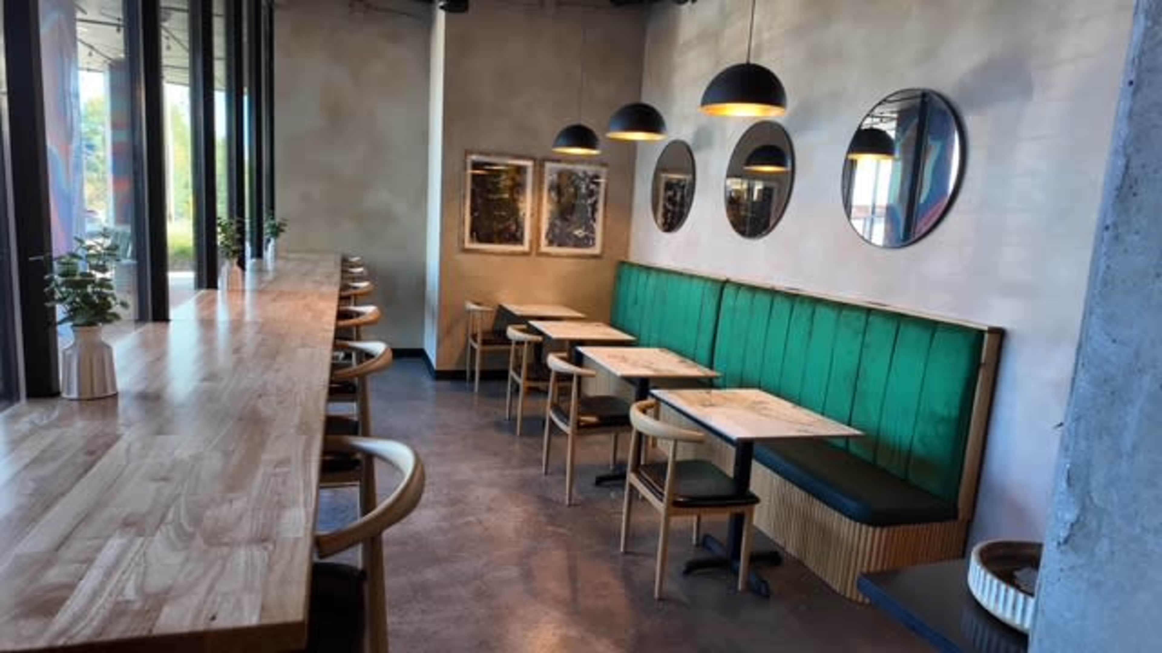 The image shows a modern cafe interior with wooden tables, green upholstered seating, and round mirrors on the walls.