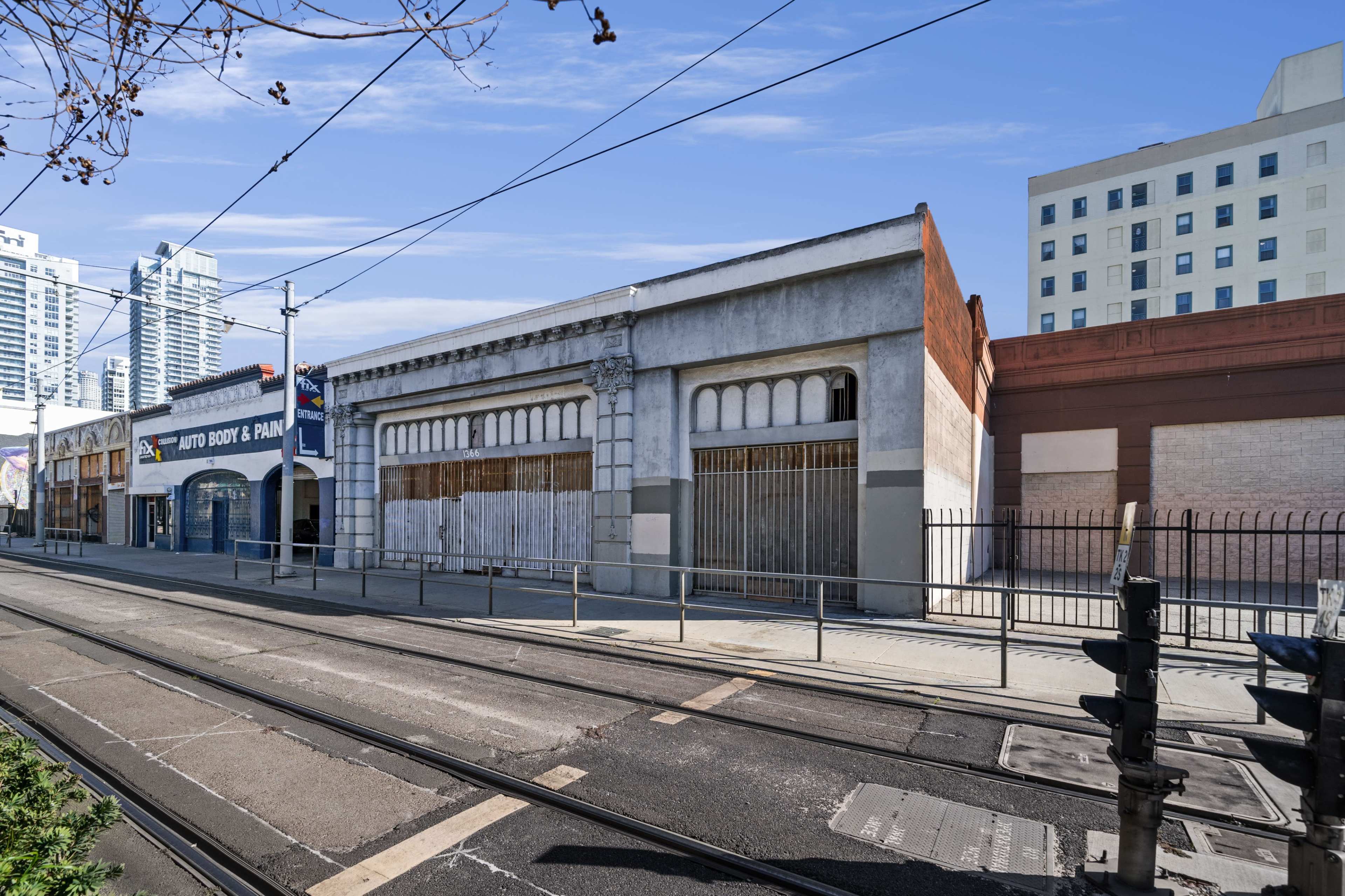 A street lined with buildings, including a boarded-up structure and an automotive shop, alongside tram tracks.
