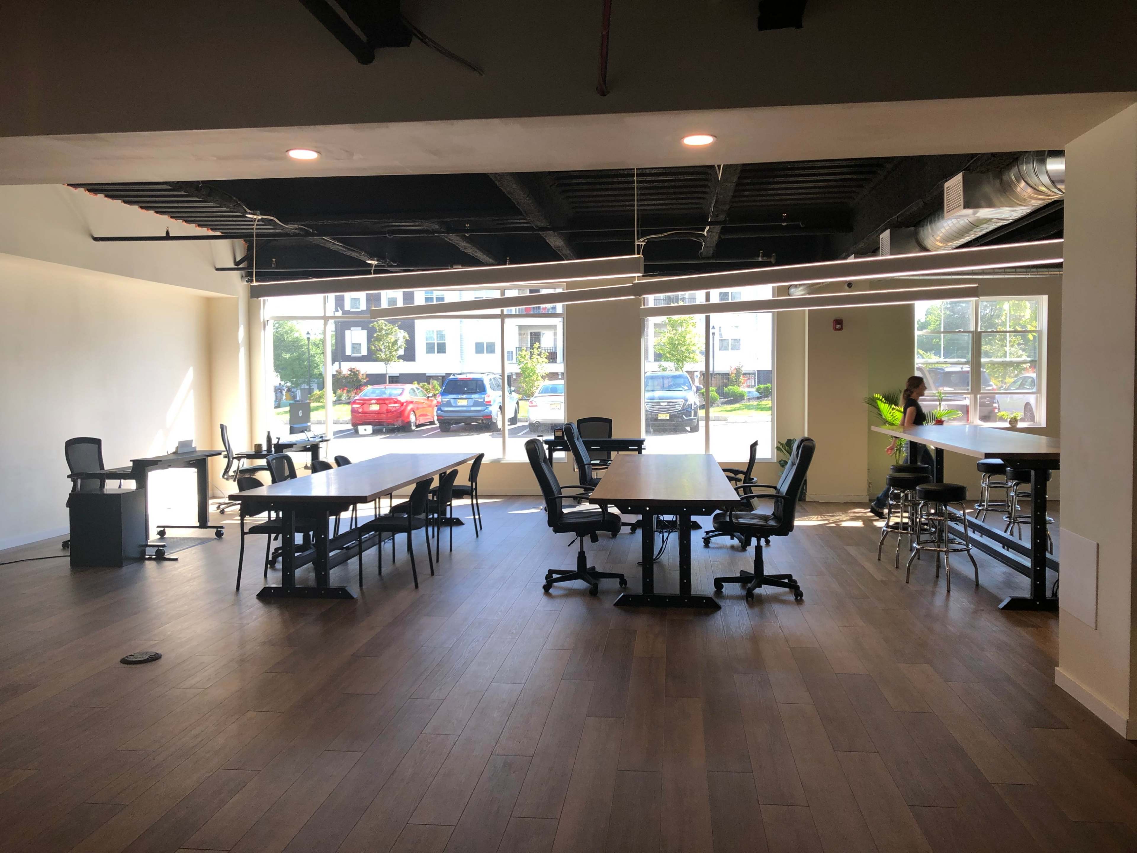 An empty modern office space with several tables and chairs arranged around large windows.