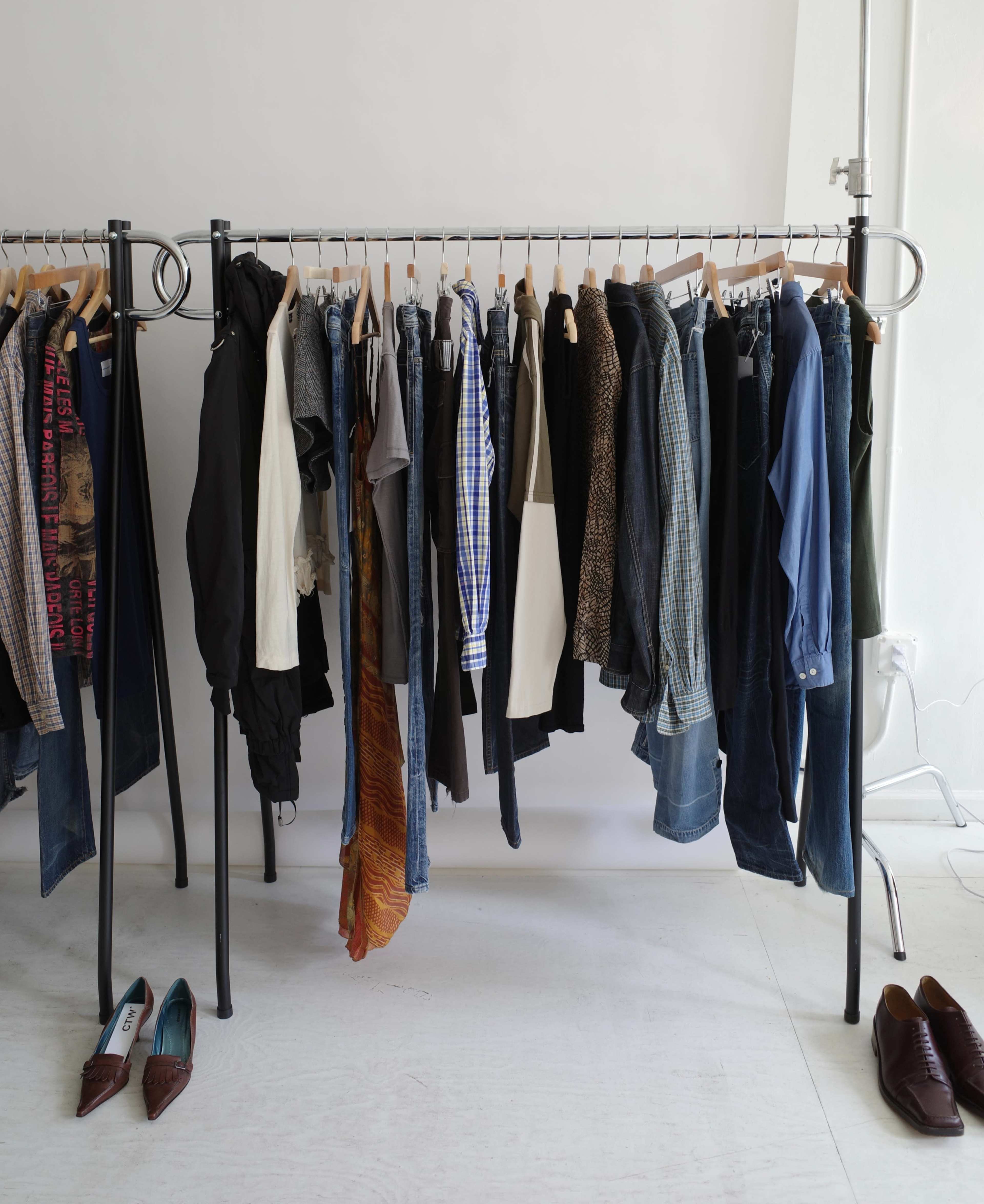 A clothing rack displays a variety of garments, including shirts, pants, and shoes, arranged neatly in a bright, minimalist setting.