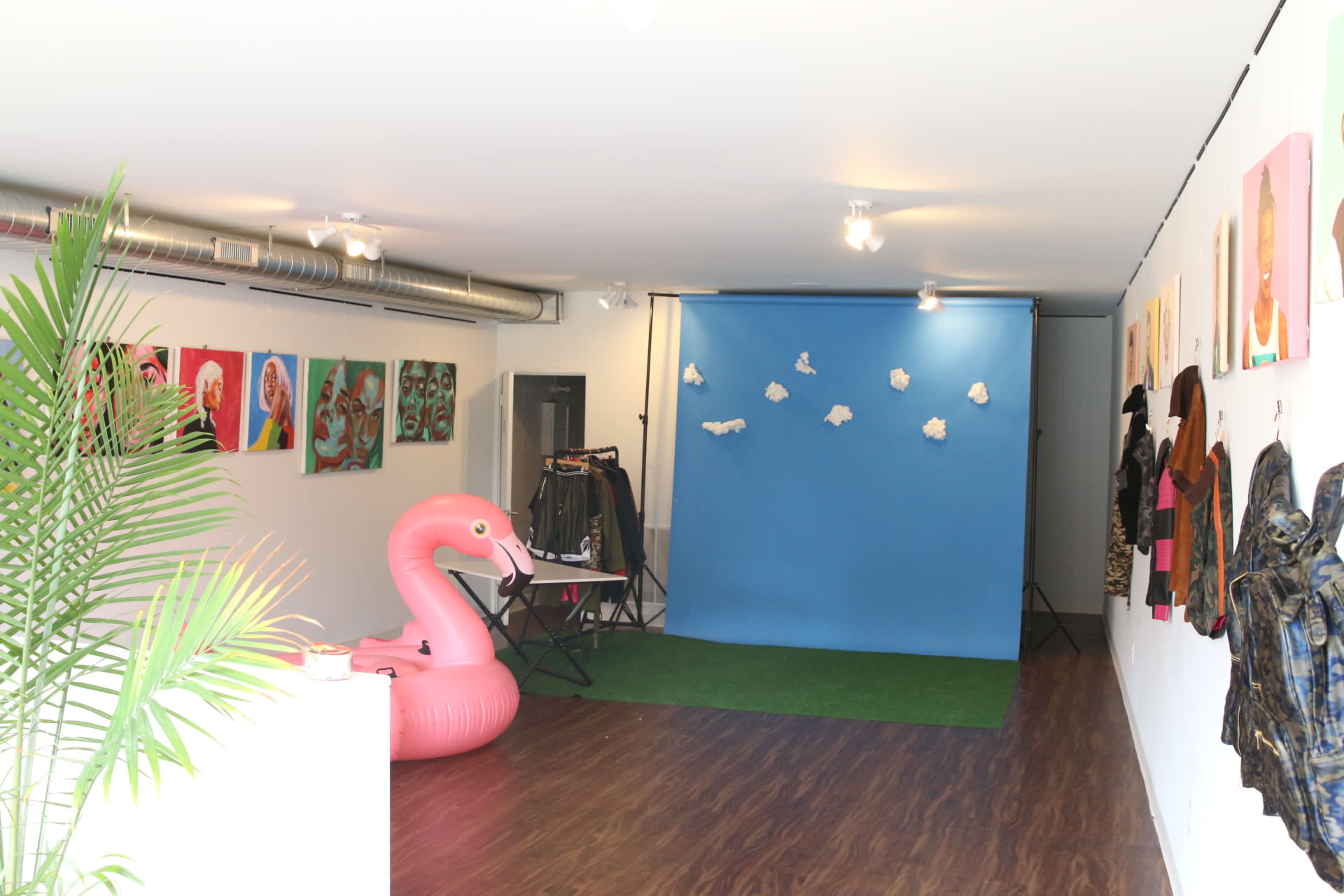 A gallery space with pink inflatable flamingo decor, a blue backdrop, and various artworks displayed on the walls.