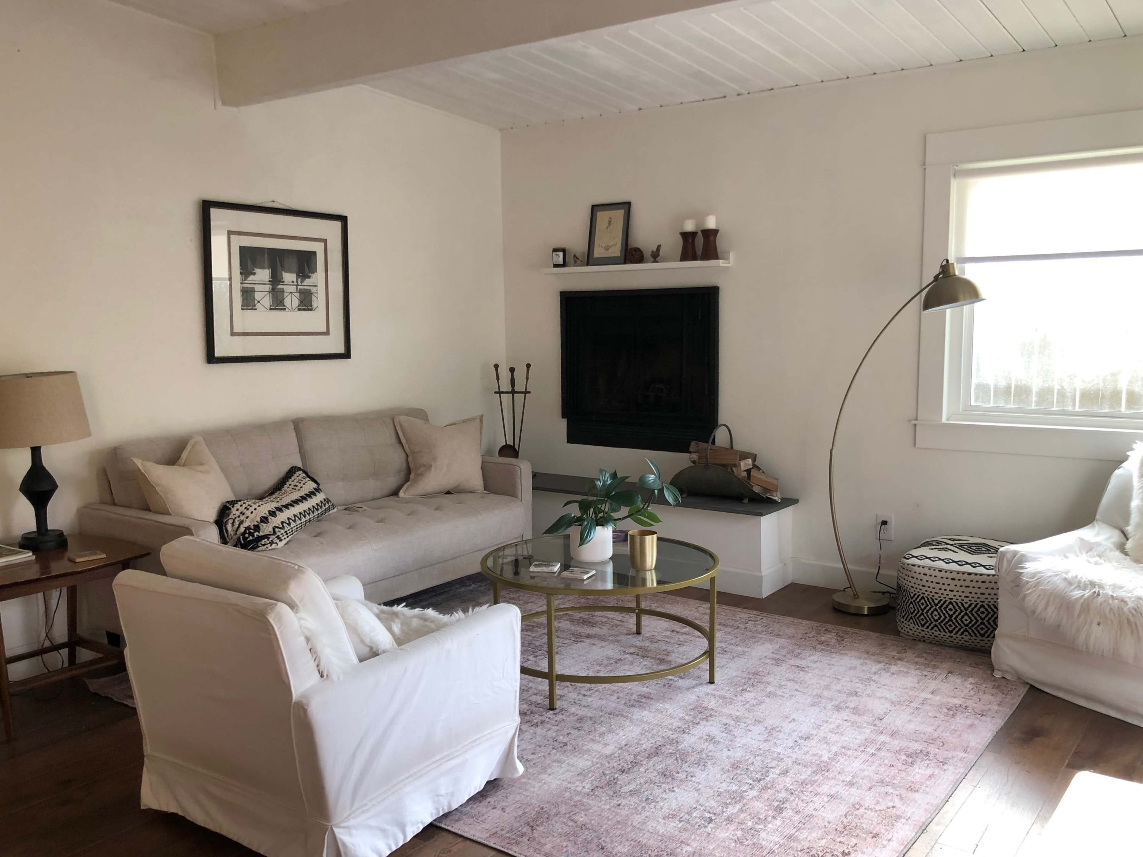 A cozy living room features a light-colored sofa, a round coffee table, and a large window, complemented by a floor lamp and a minimalist decor.