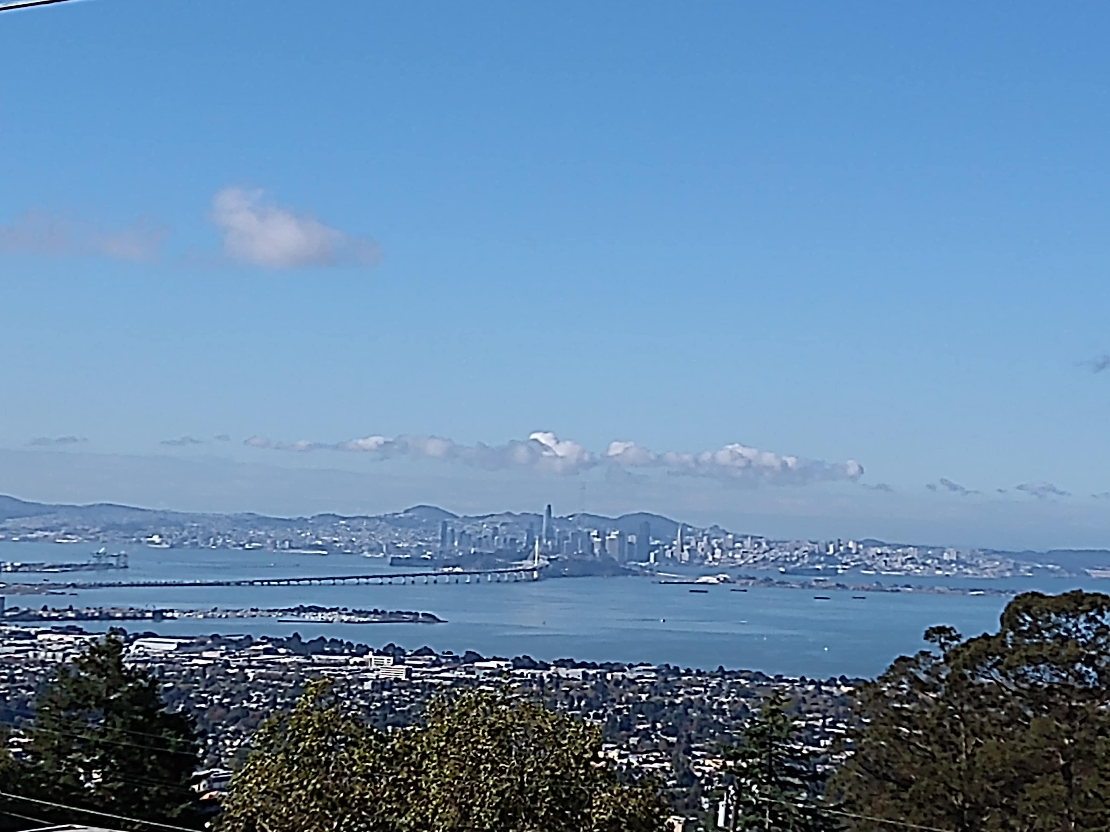 A view of the San Francisco skyline across the water, with hills and clouds in the background.