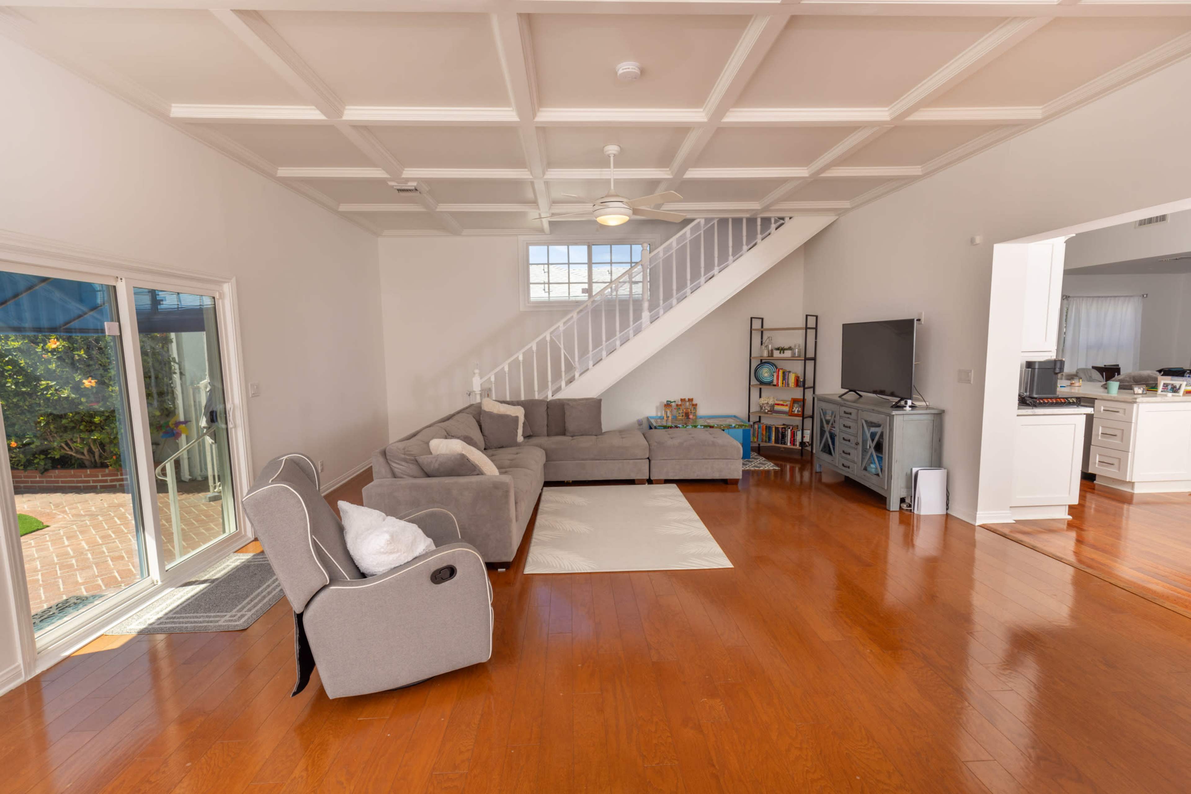 The image shows a spacious living room with a sectional sofa, a flat-screen TV, and an open staircase leading to the upper level.