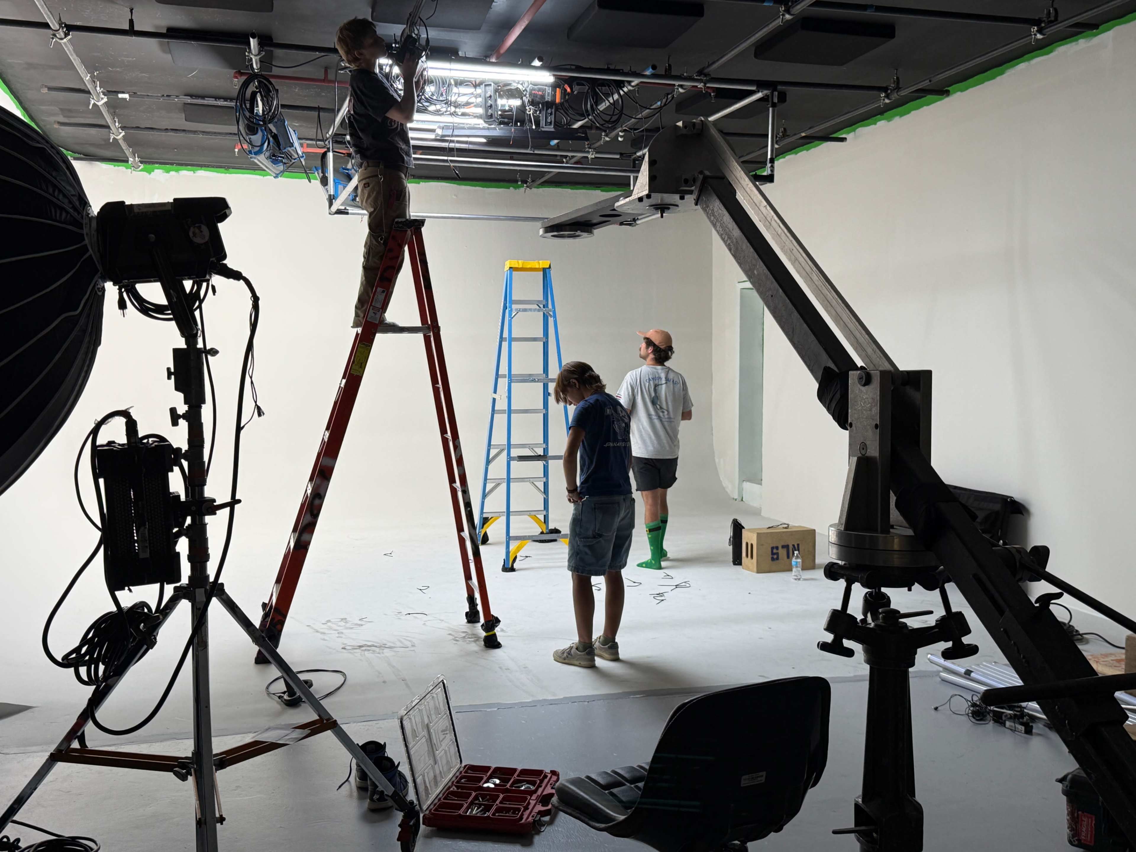A film set is being prepared with a crew setting up equipment and adjusting lighting in a blank studio space.