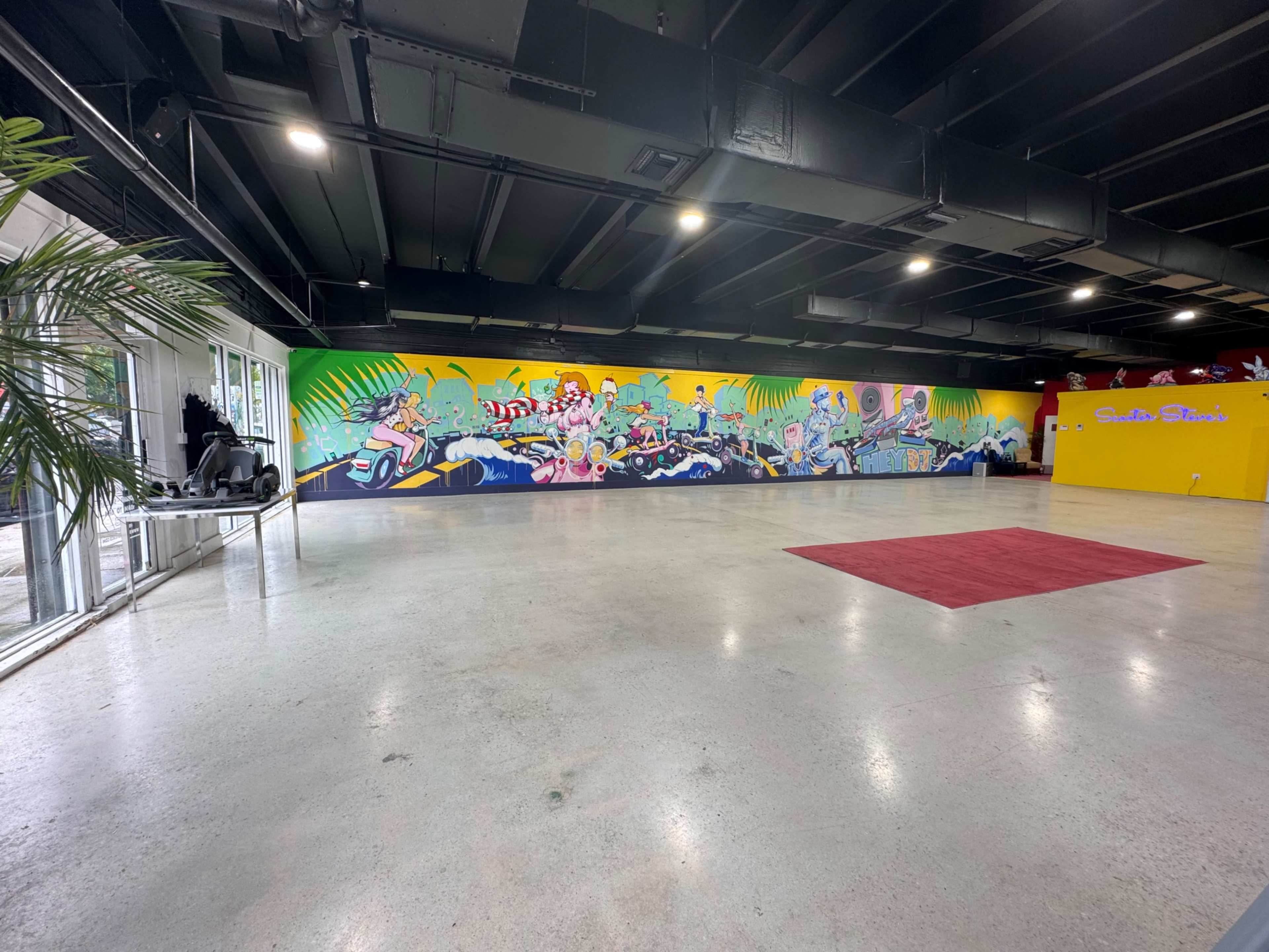 An industrial-style indoor space featuring a colorful mural on one wall and a yellow wall on the opposite side.