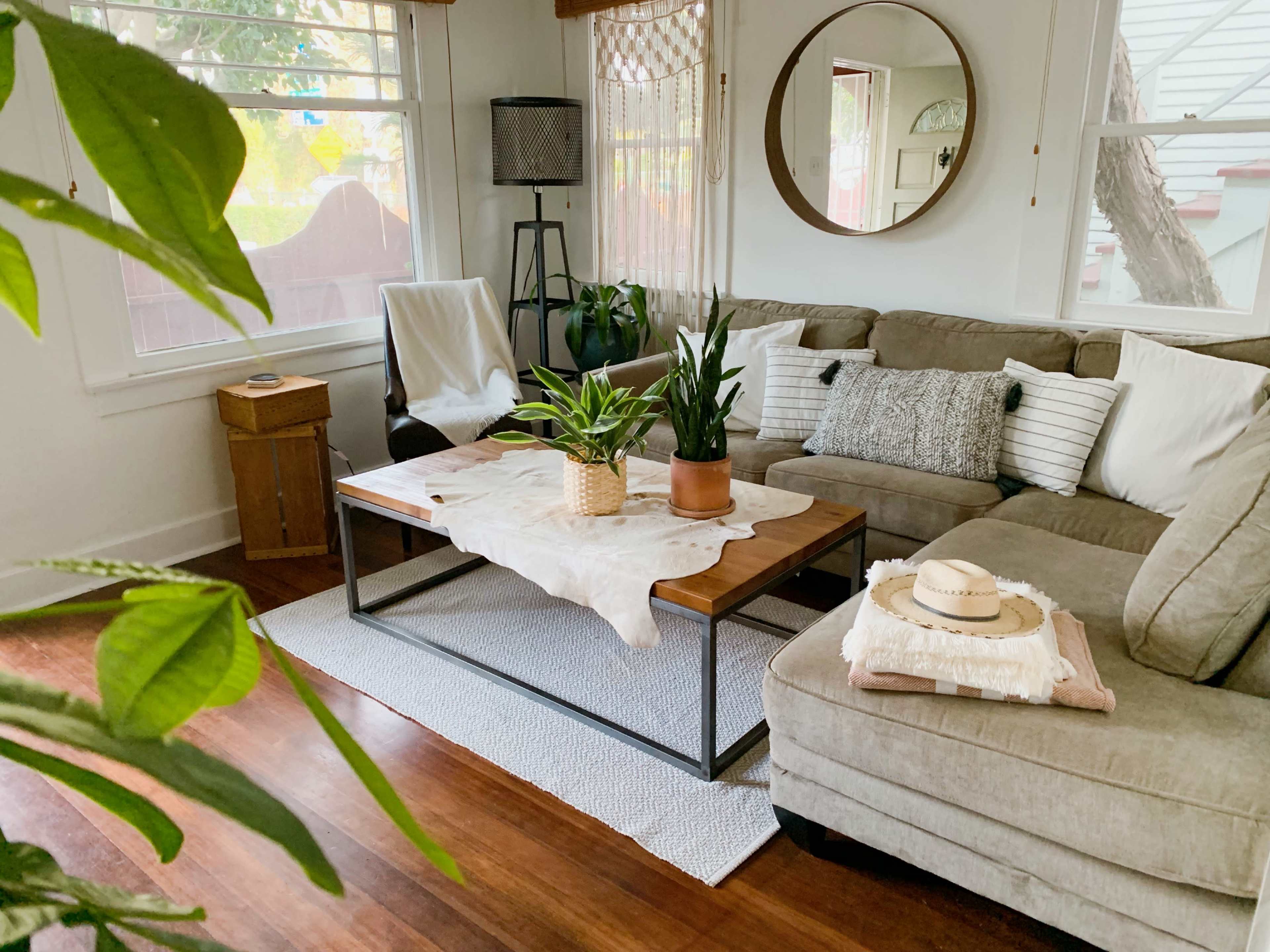 A cozy living room features a sectional sofa, a wooden coffee table with plants, and natural light coming through a window.