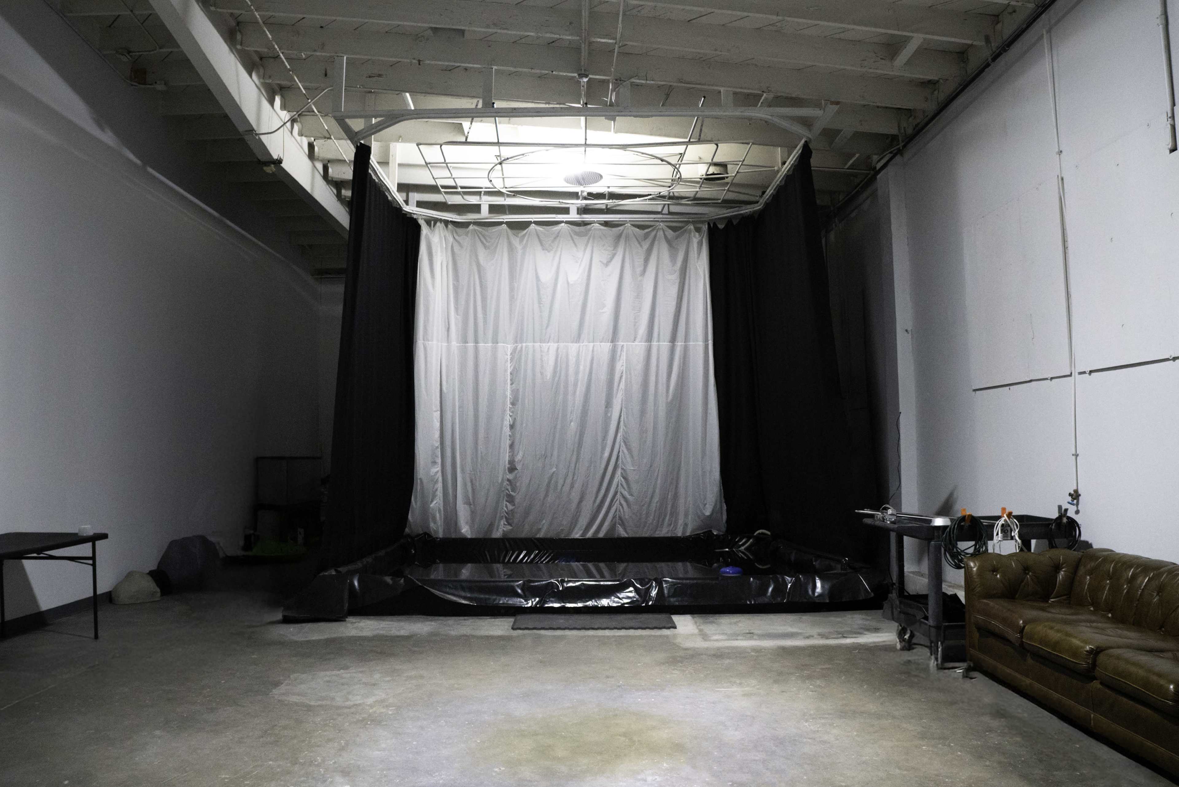 The image shows a large, empty space with a black backdrop and a shallow pool in the center, while a brown sofa sits along one side.