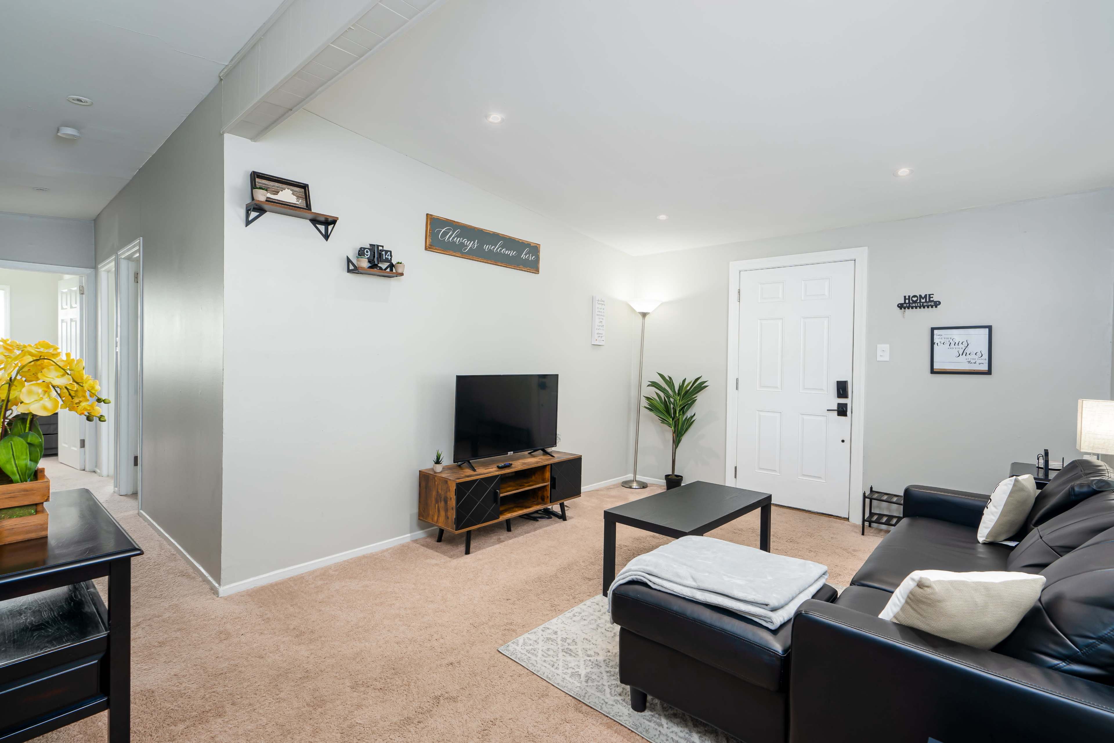 The image shows a cozy living room with a television on a stand, a dark sofa, and a door leading outside.