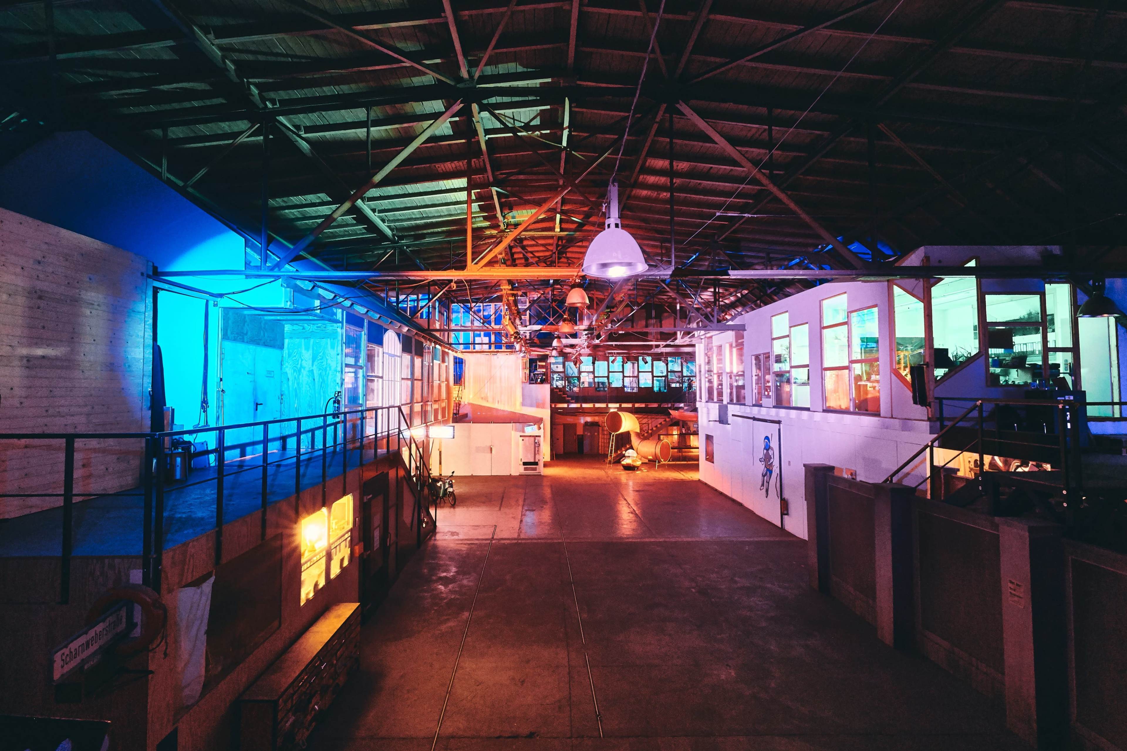 A spacious industrial interior with colorful lighting, featuring sections of walls and large windows in a warehouse-like setting.
