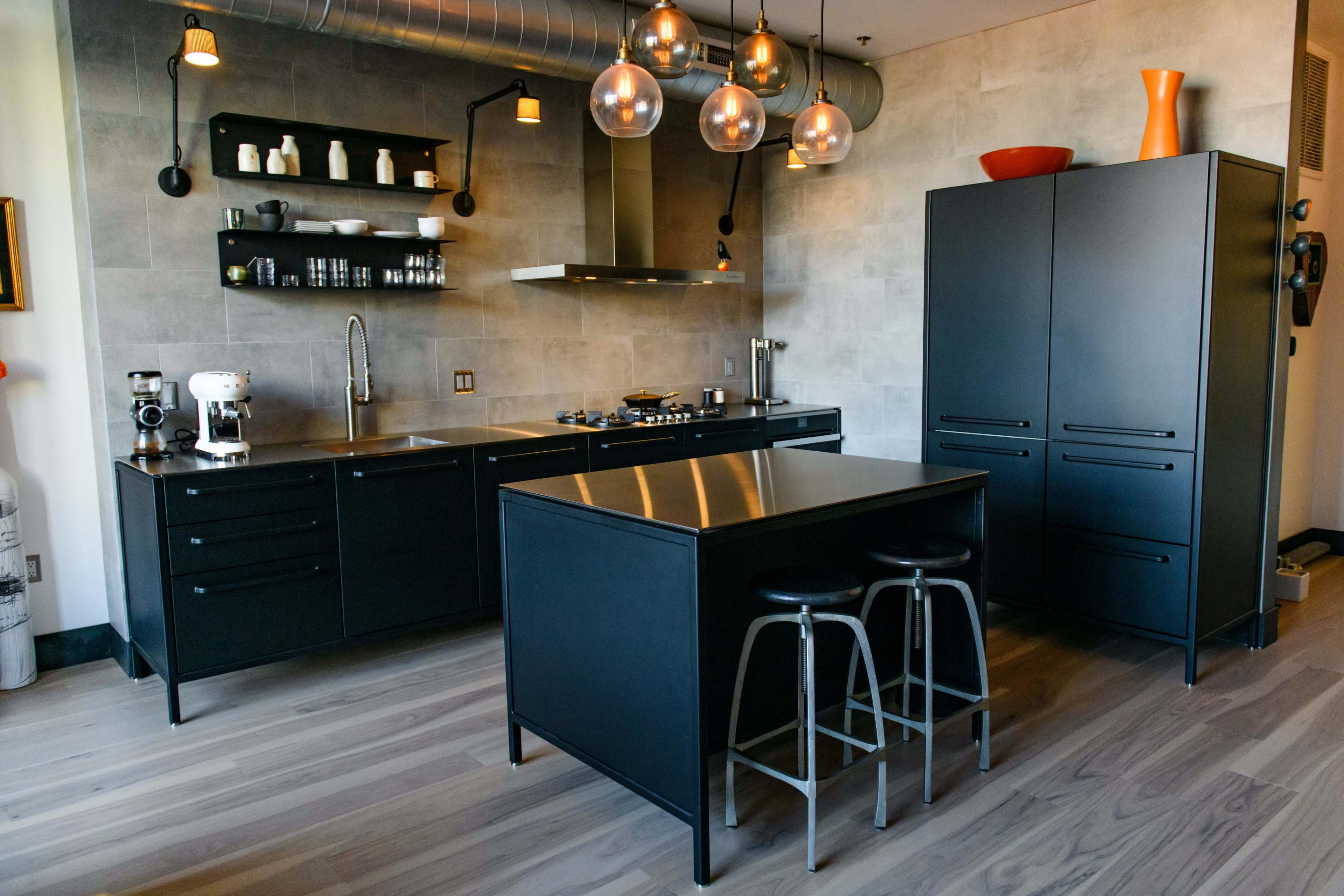 The image shows a modern kitchen featuring black cabinetry, a central island with seating, and industrial-style lighting.