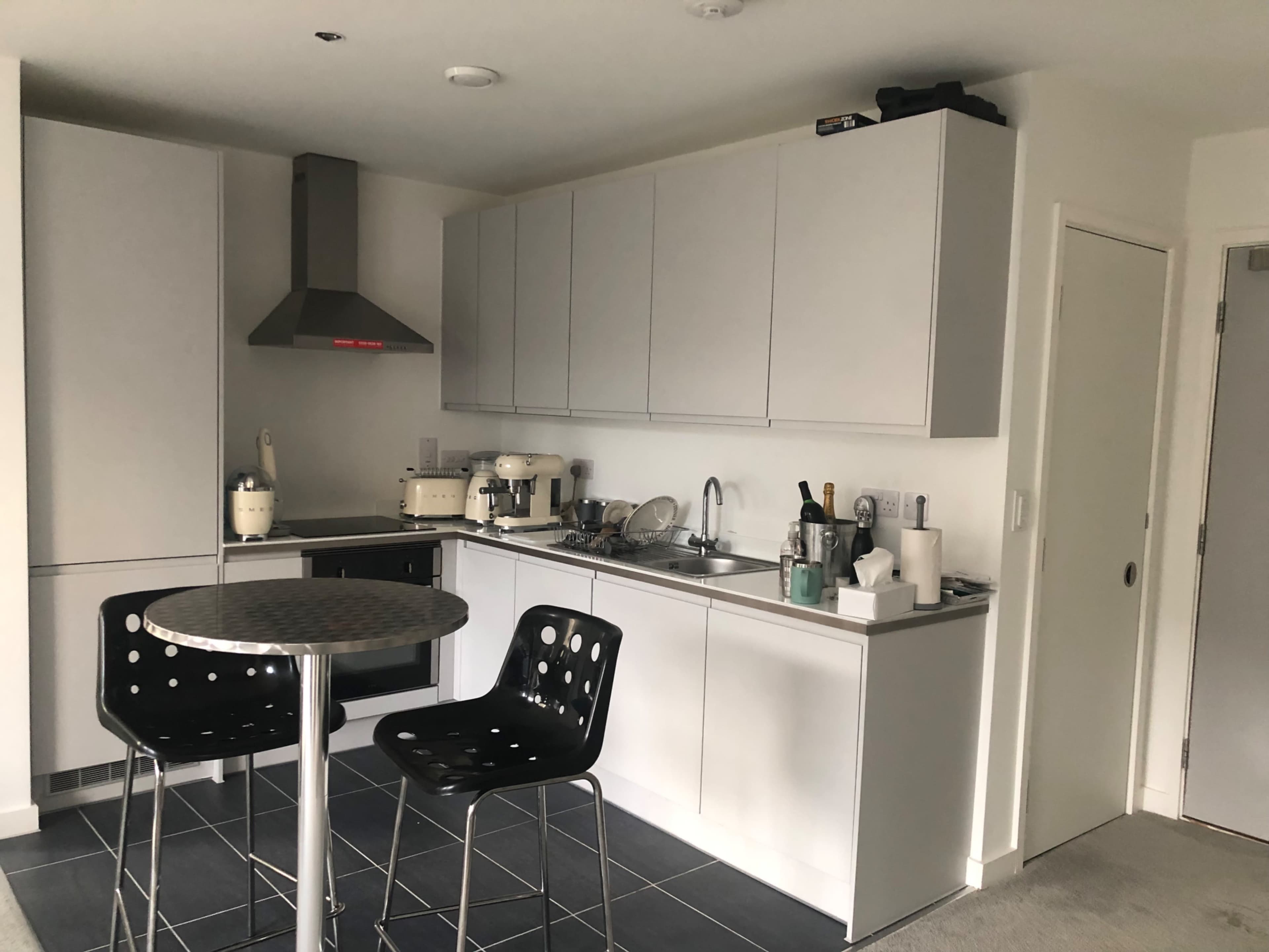 The image shows a modern kitchen featuring gray cabinets, a stainless steel range hood, and a round table with two black chairs.