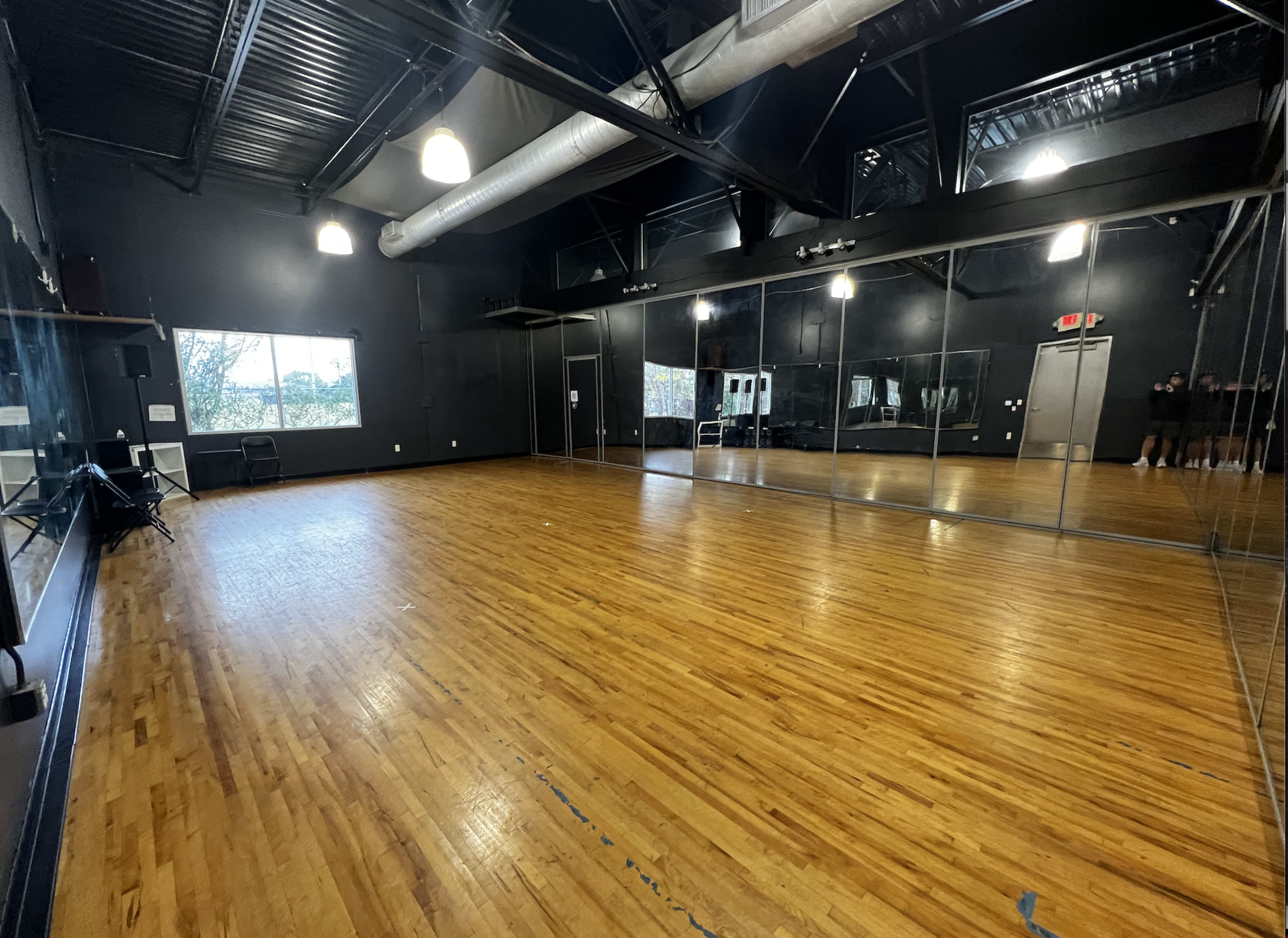 An empty dance studio with wooden flooring and large mirrors lining one wall.