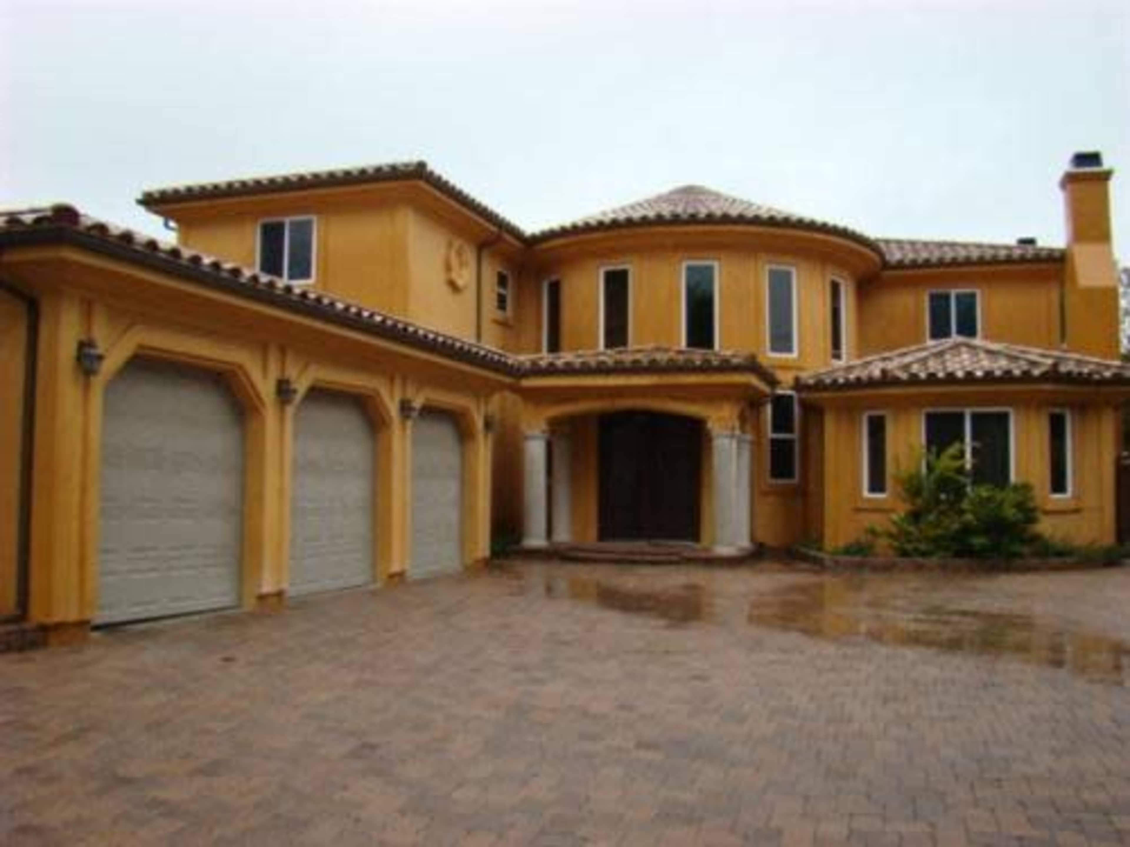 A large, yellow-stucco house with a tiled roof and a three-car garage.