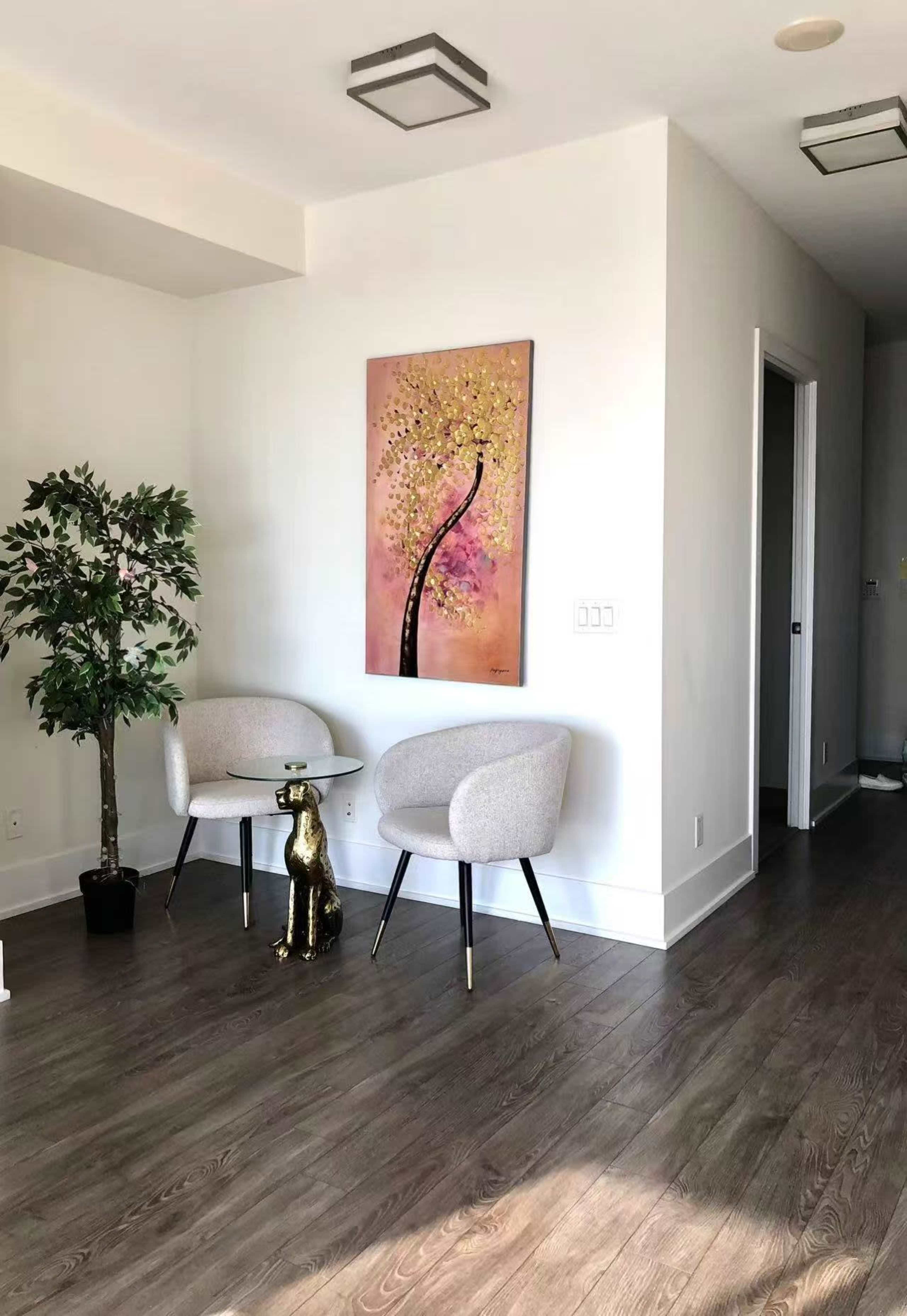 The image shows a modern room with two chairs facing an art piece on the wall, featuring a tree design, alongside a decorative plant and a dog statue.