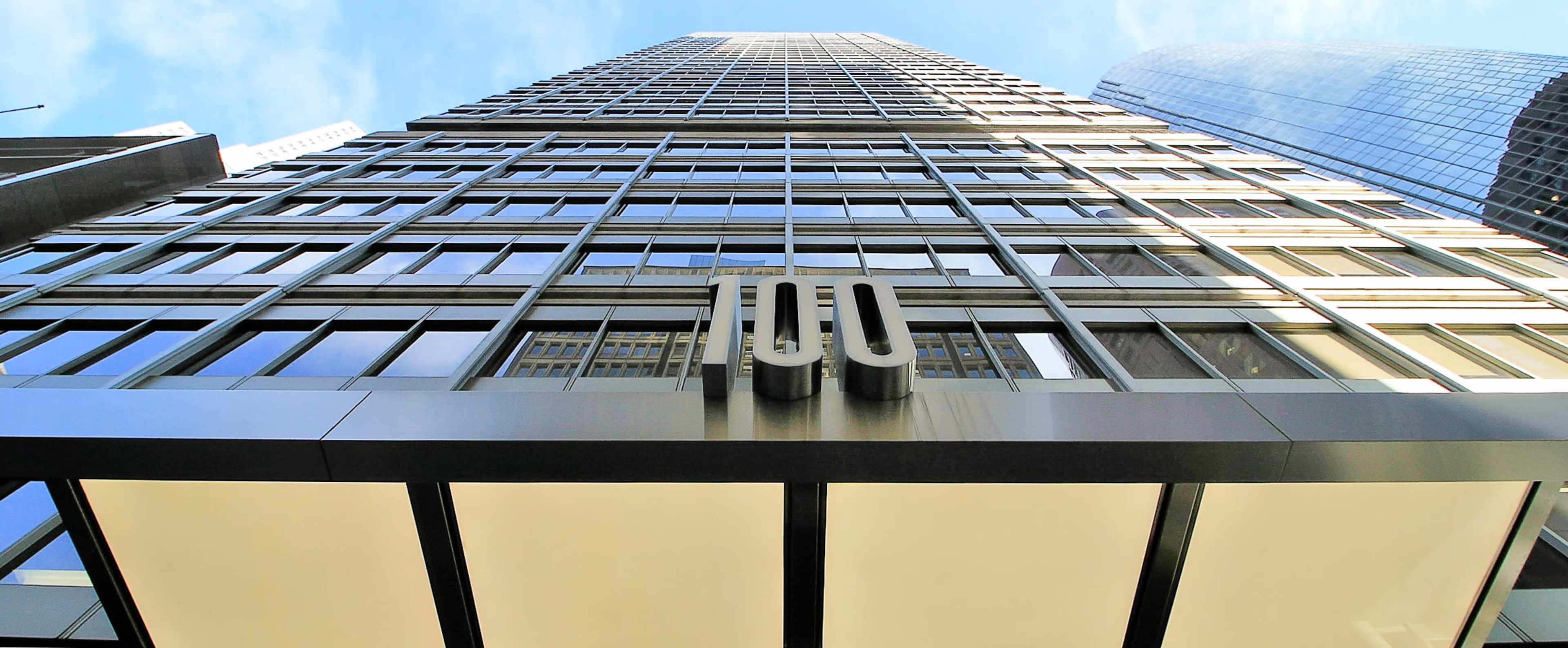 The image shows a tall modern building viewed from the ground level, with a prominent "100" sign displayed on its facade.