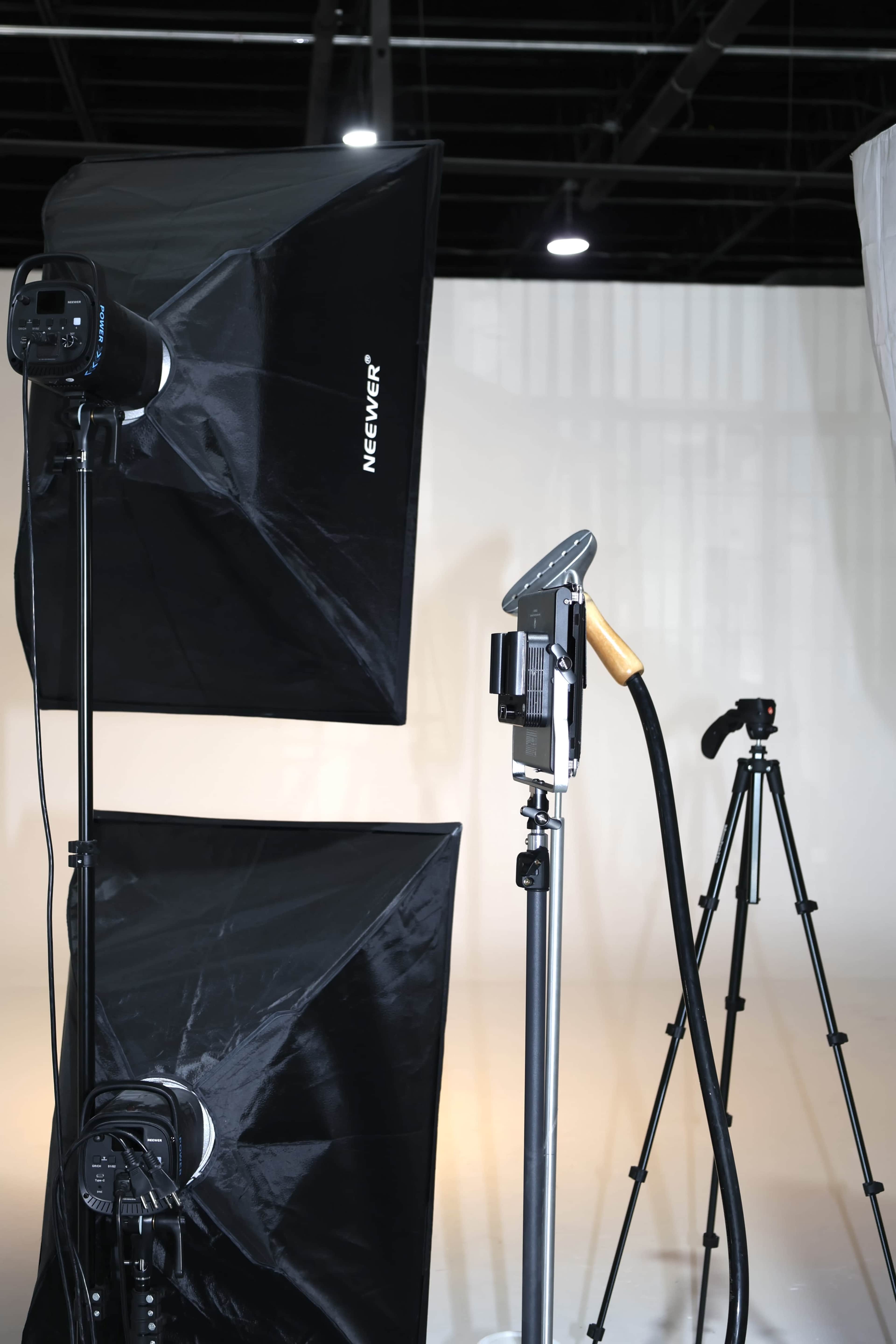 The image shows photography lighting equipment, including softboxes and a tripod, set up in a studio space with a plain background.