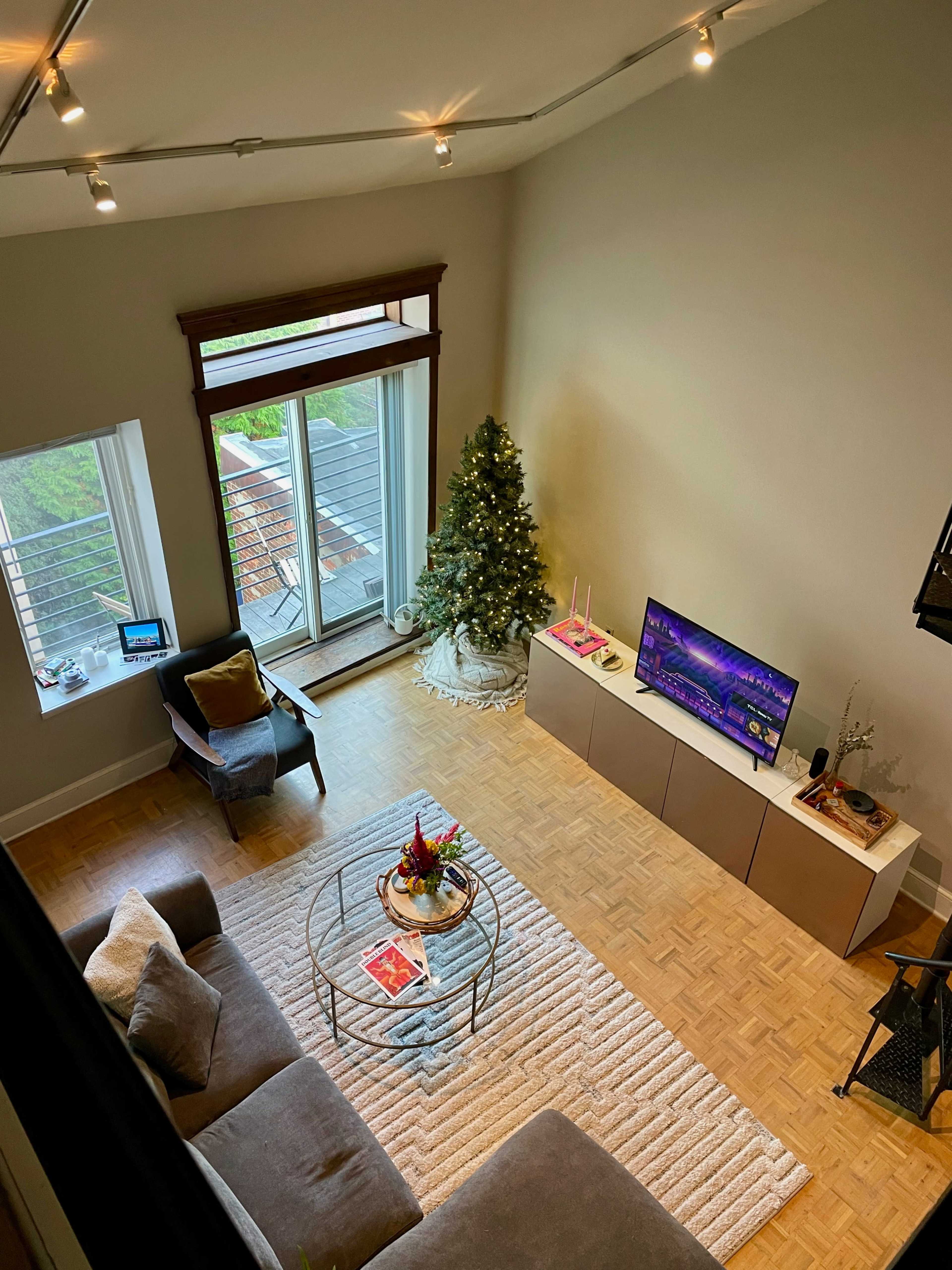 A neatly arranged living room featuring a Christmas tree, a television, a coffee table with decorations, and large windows that open to a balcony.
