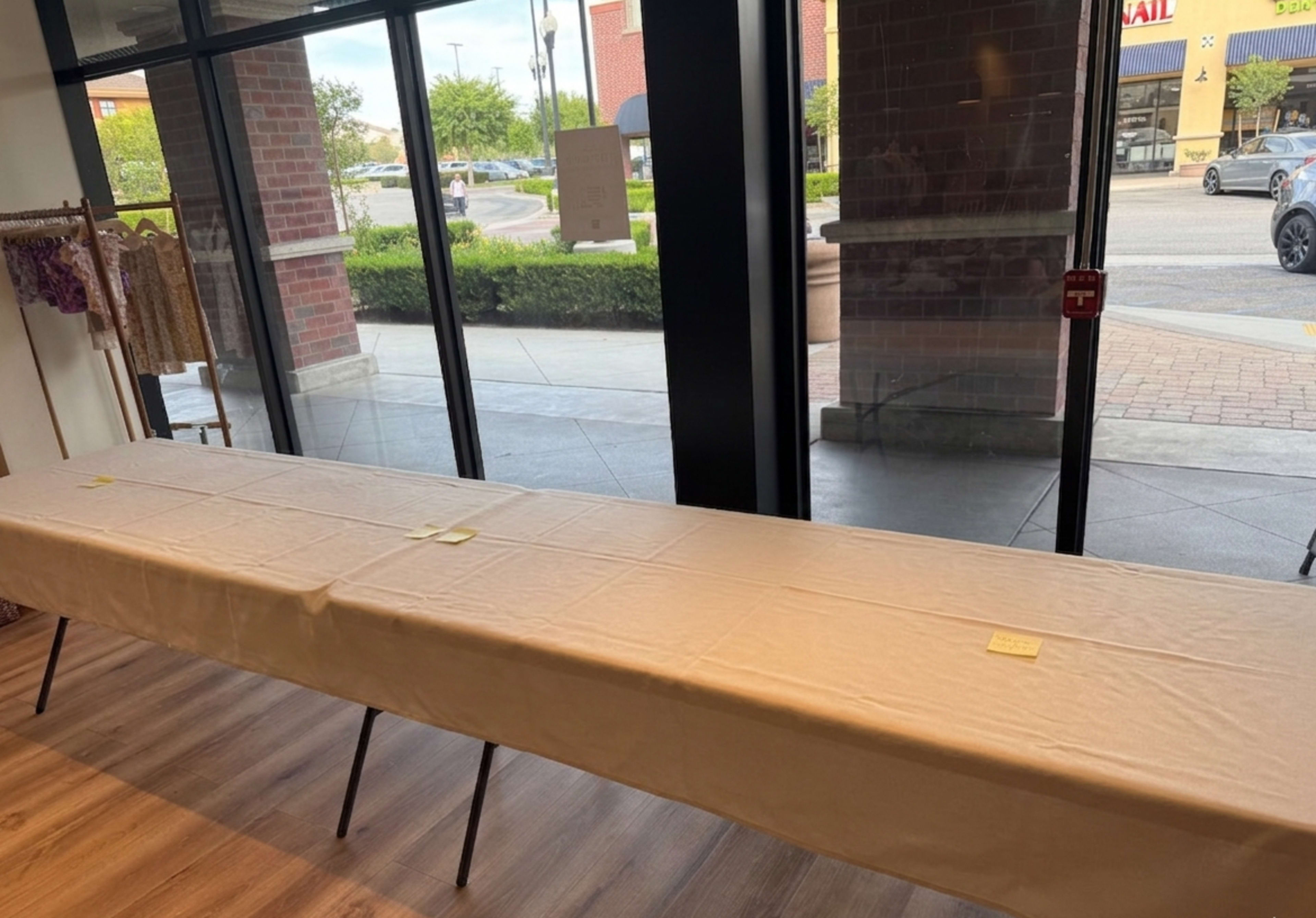 A long, covered table sits in front of a large window, with a view of a shopping area outside.