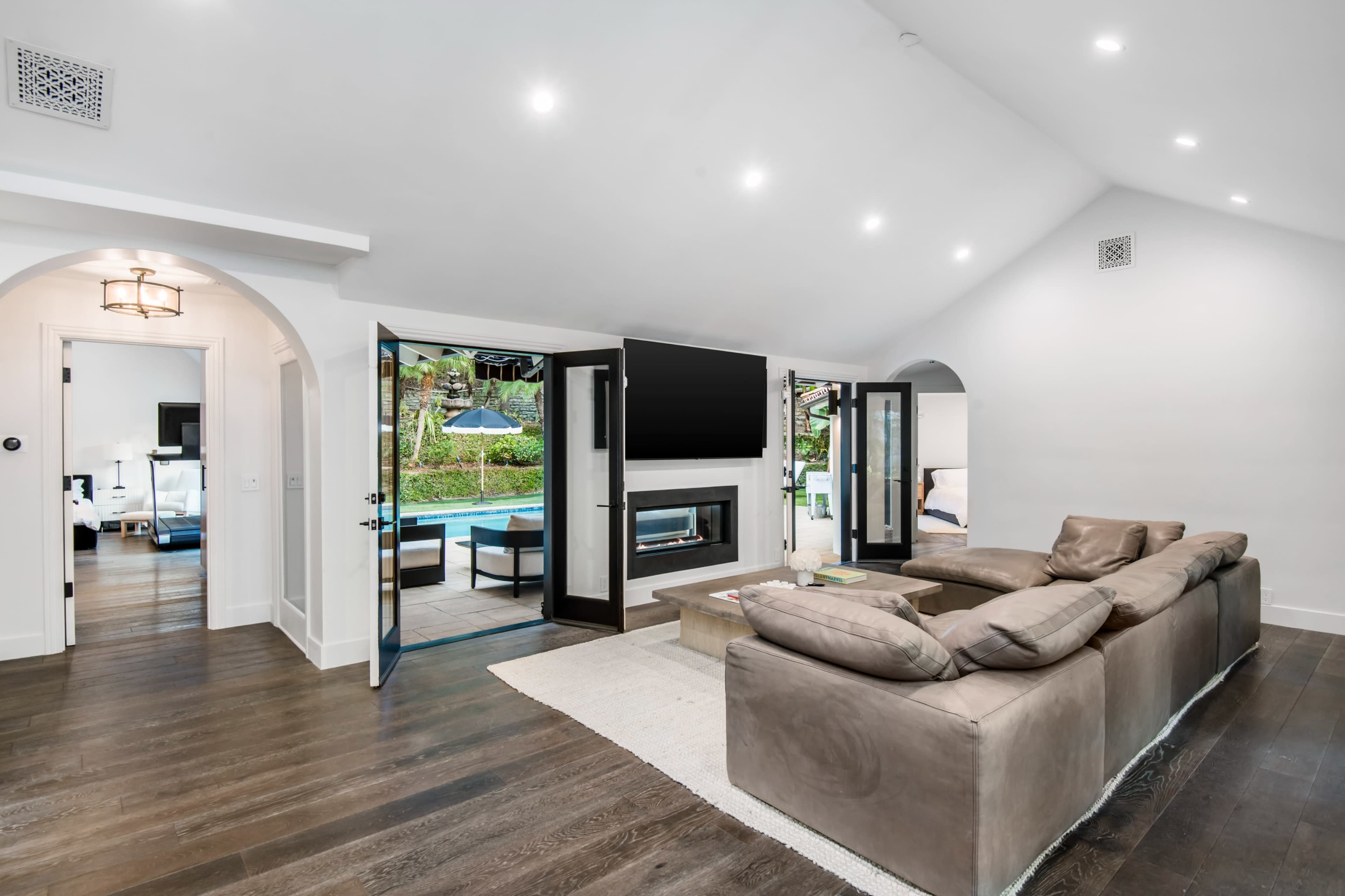 A modern living room with large open doors leading to a pool area, featuring a sectional couch and a fireplace.
