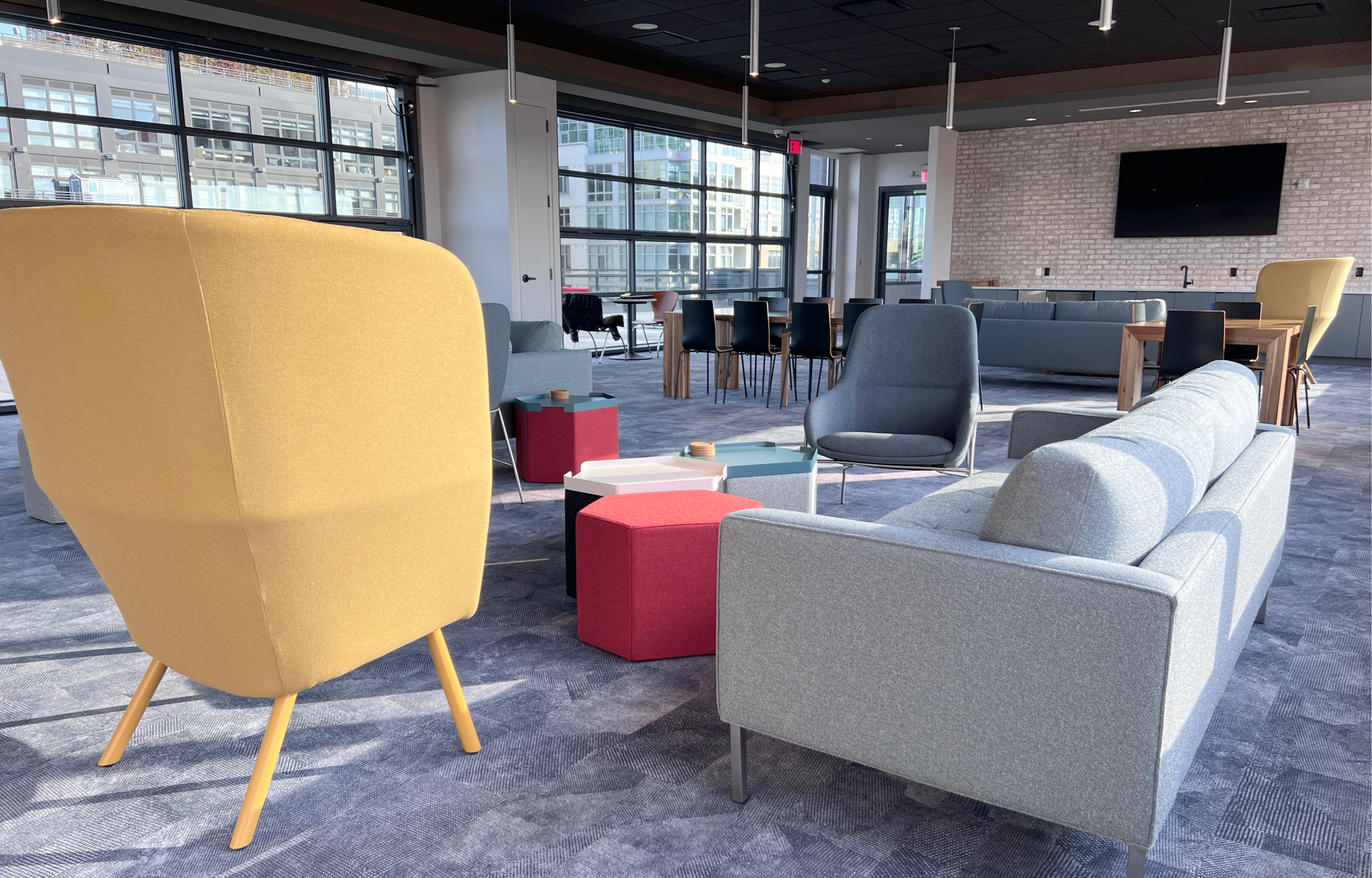 A modern lounge area featuring various colorful seating arrangements, including a yellow chair, a gray sofa, and red and blue coffee tables.