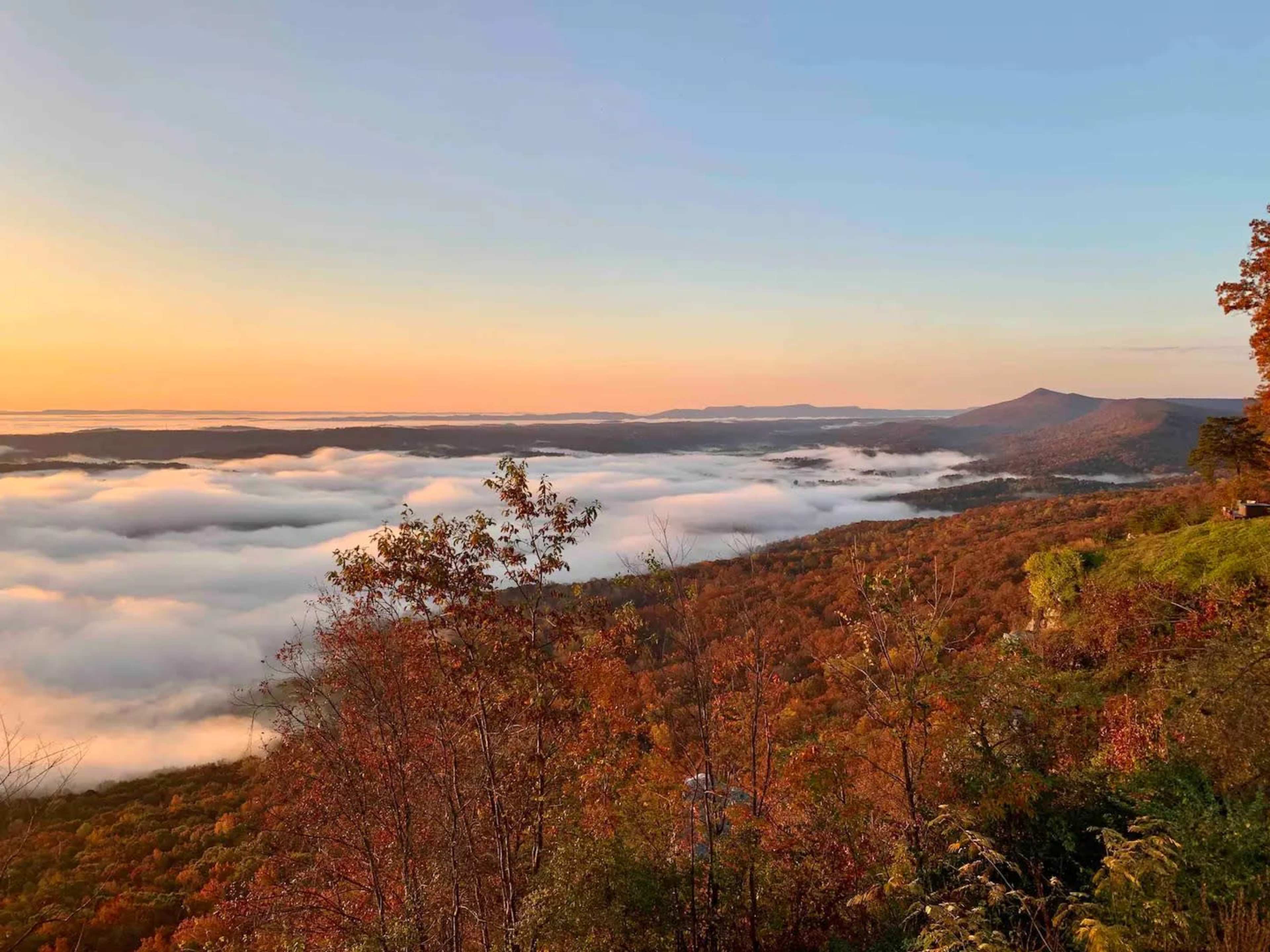 The scene depicts a valley filled with fog, surrounded by autumn foliage and mountains under a clear sky at sunrise.