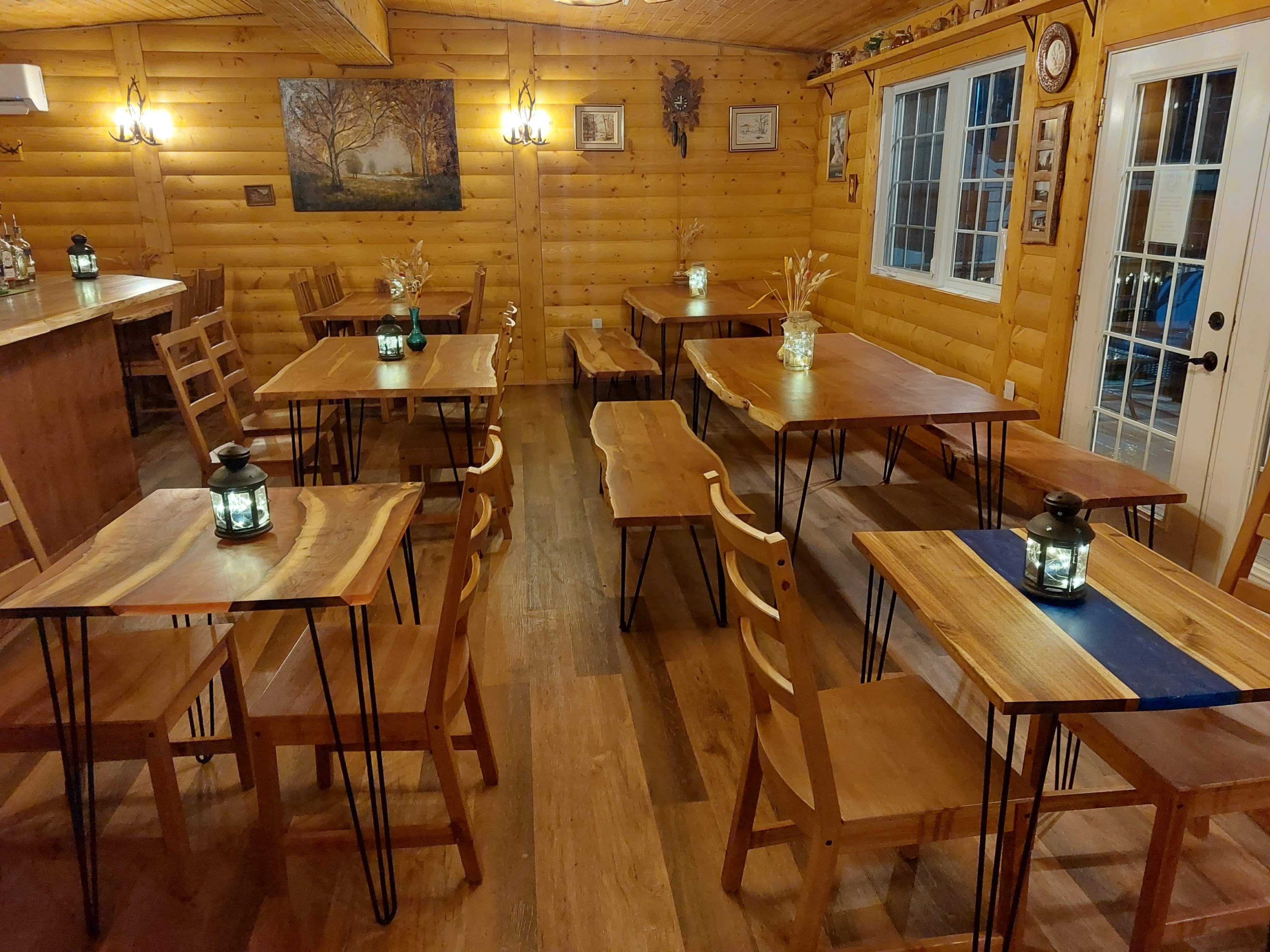 A wooden interior space with several tables and chairs arranged neatly around lanterns, along with a bar area and large windows.