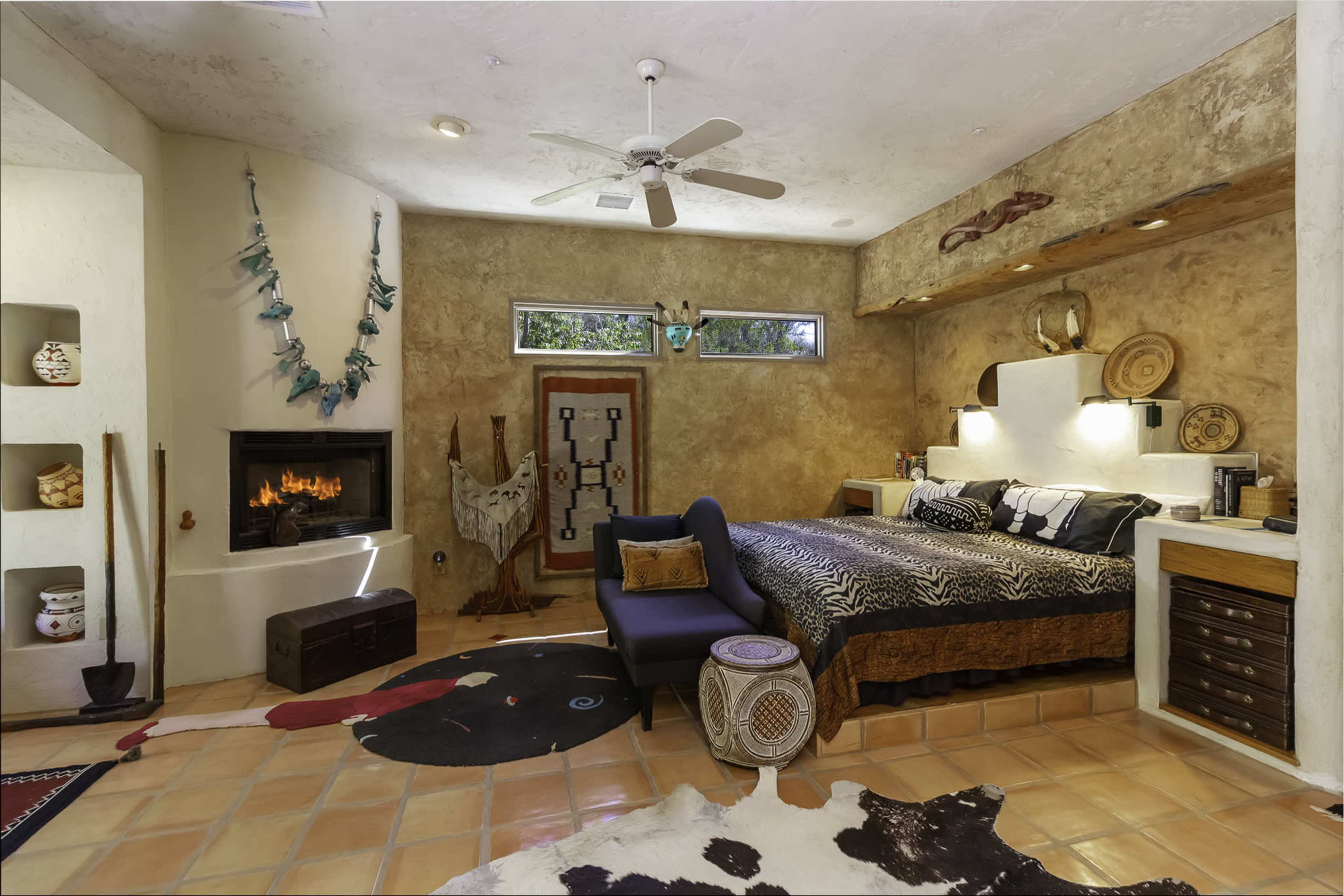 A rustic bedroom with a bed, a modern fireplace, decorative wall art, and earthy tones throughout.