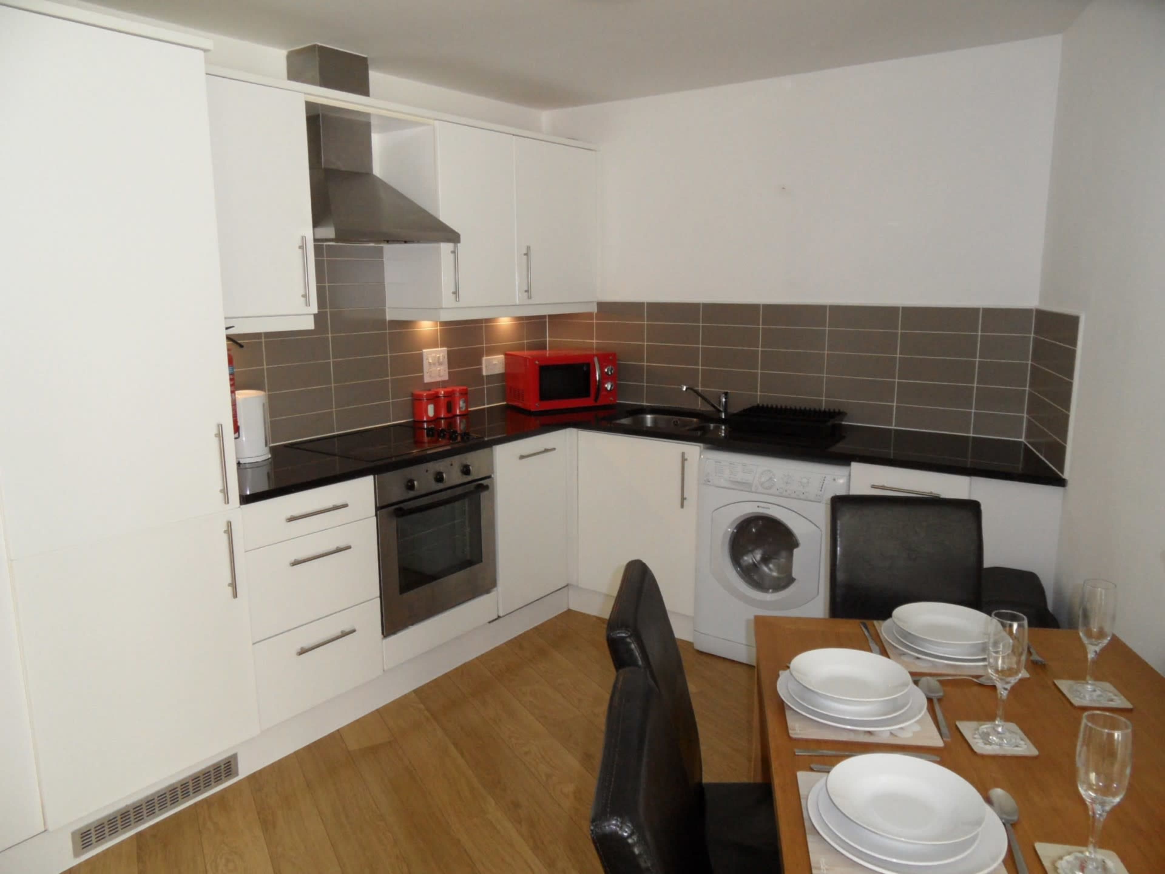 A modern kitchen with white cabinets, stainless steel appliances, and a wooden dining table set with plates and glasses.