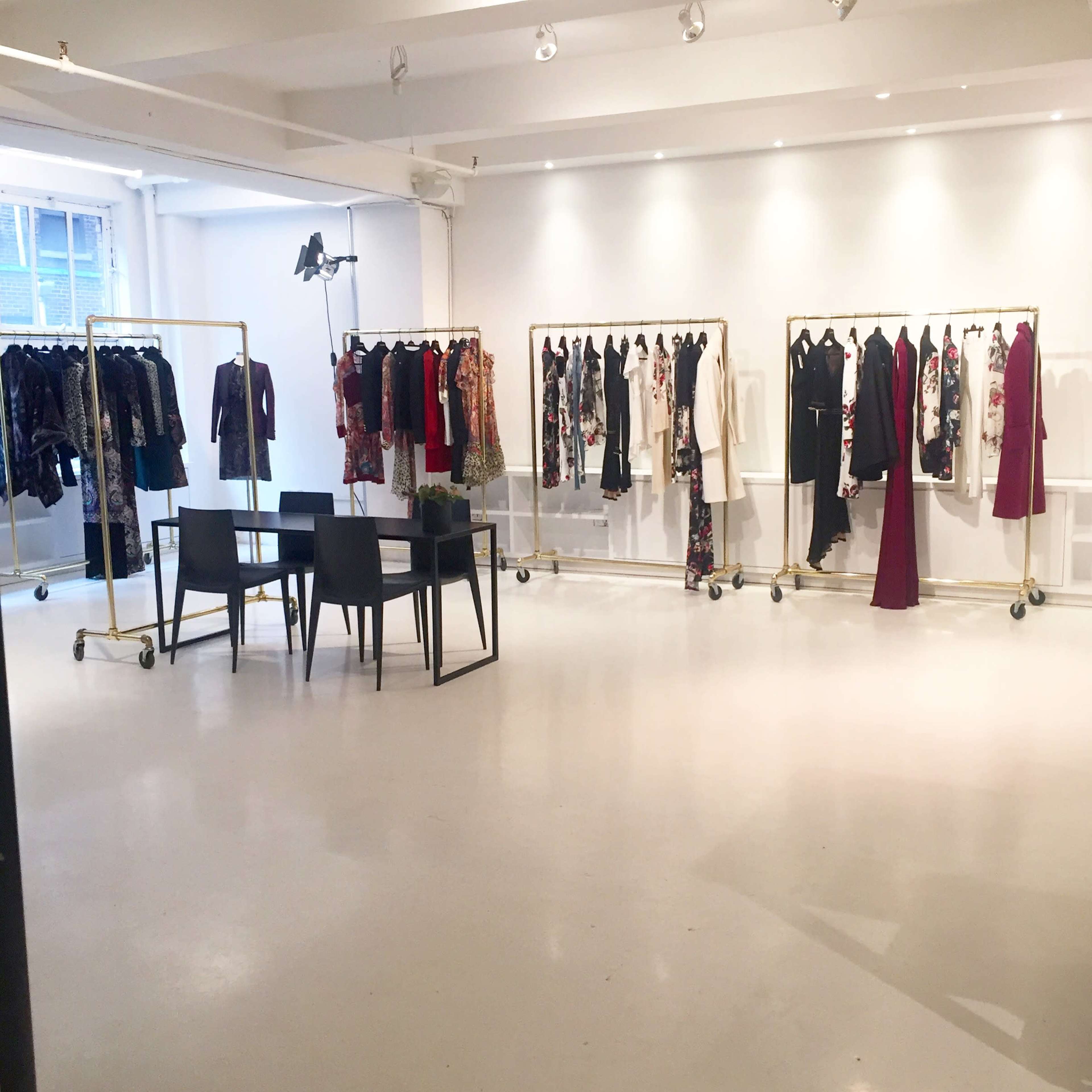 A spacious clothing display area with racks of dresses arranged on the left side and a table with chairs positioned in the center.