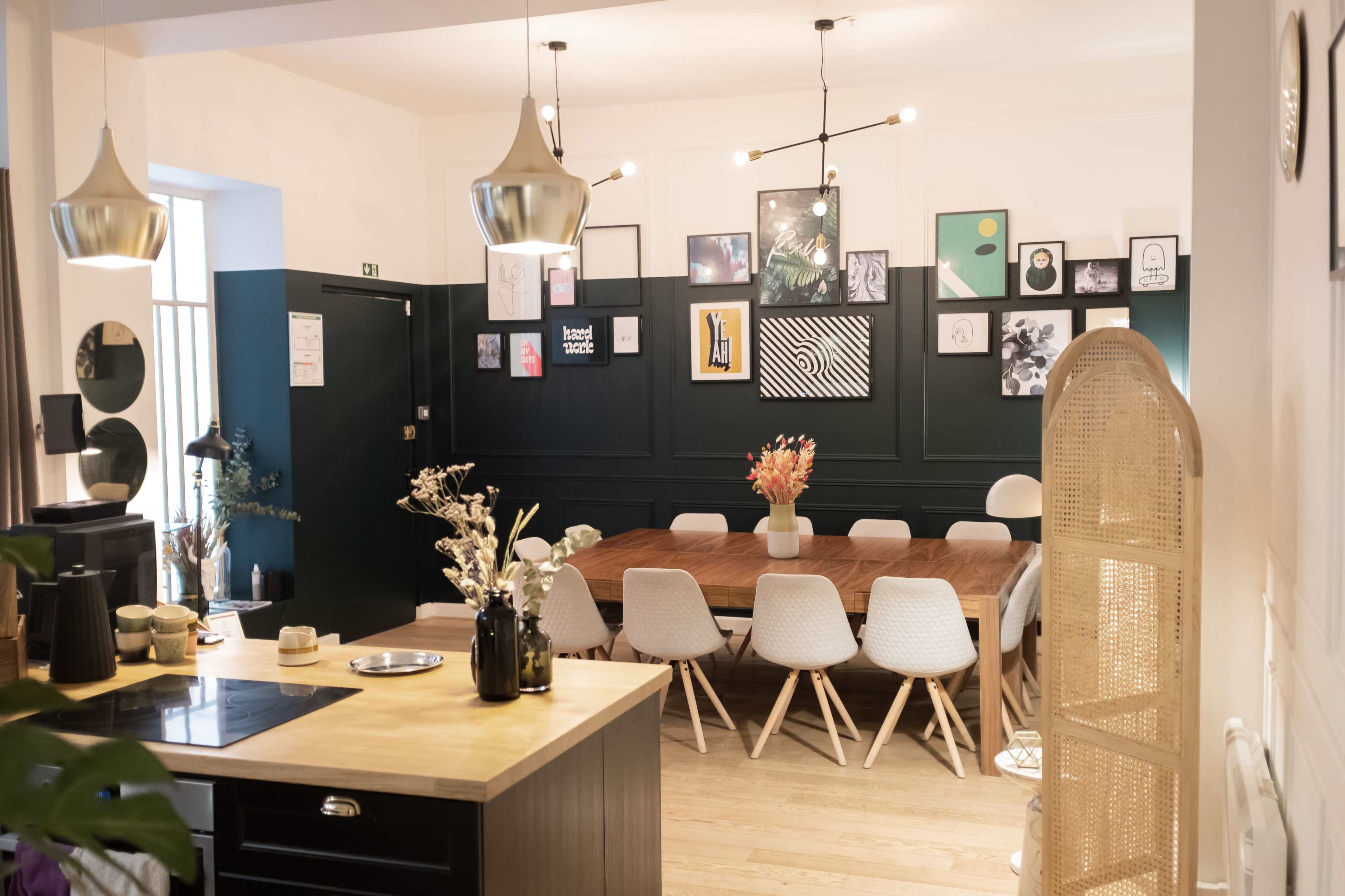 A modern dining area features a wooden table surrounded by white chairs, with a gallery wall of framed art and stylish pendant lights overhead.
