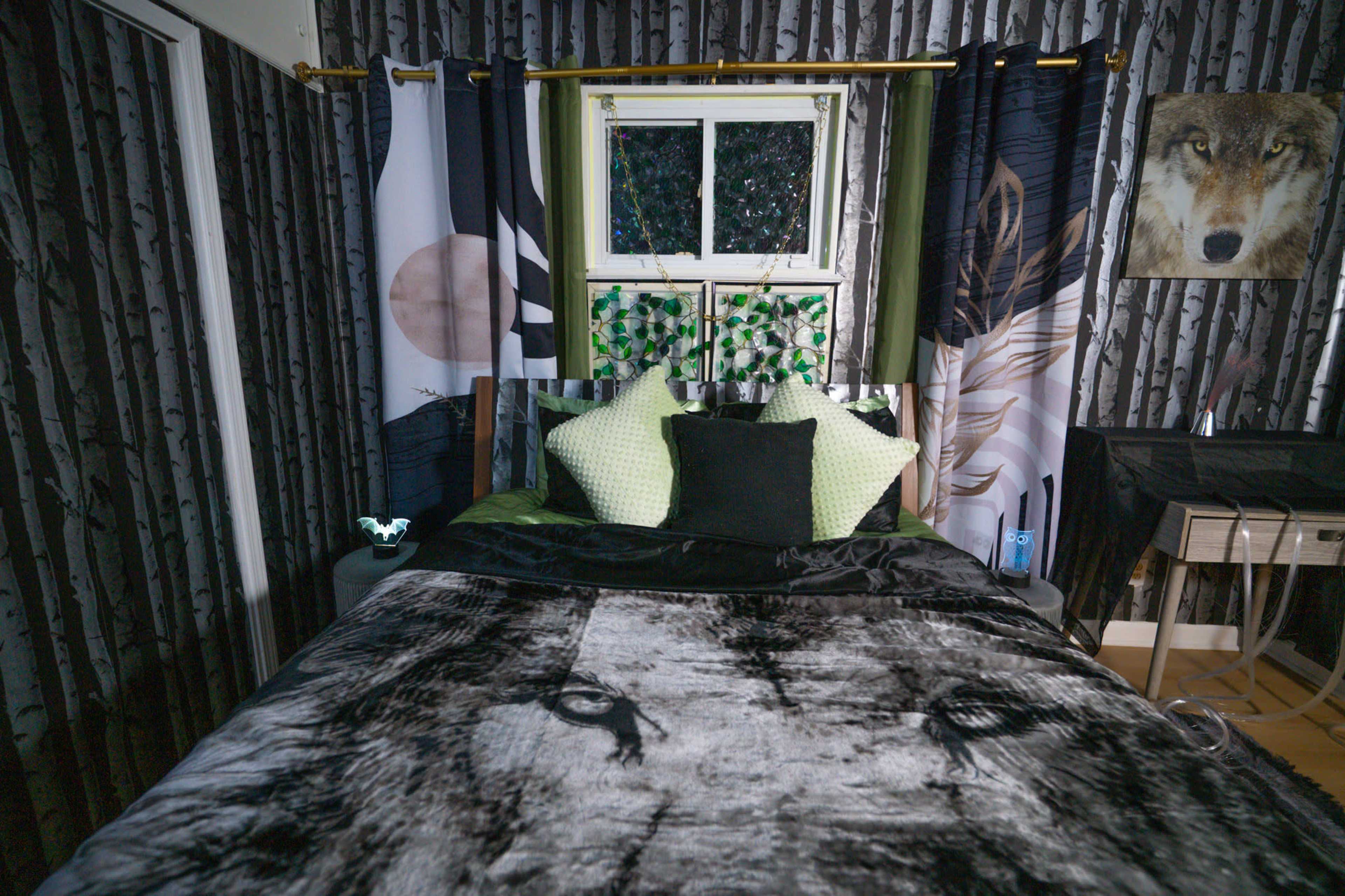 The room features a bed with a large black and white animal-themed blanket, accented by decorative pillows, surrounded by dark wallpaper depicting trees and wildlife-themed decor.