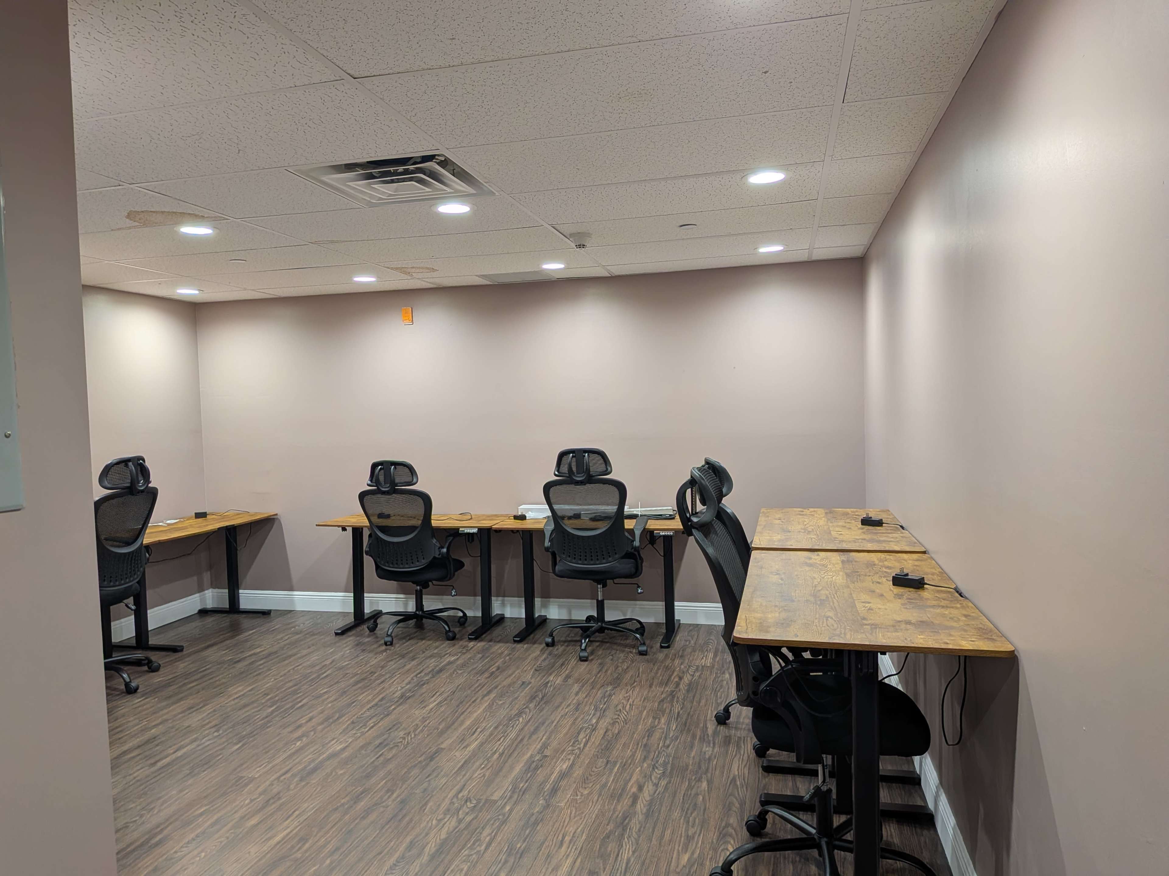 The image shows an empty office space with several wooden desks and ergonomic chairs arranged along the walls.