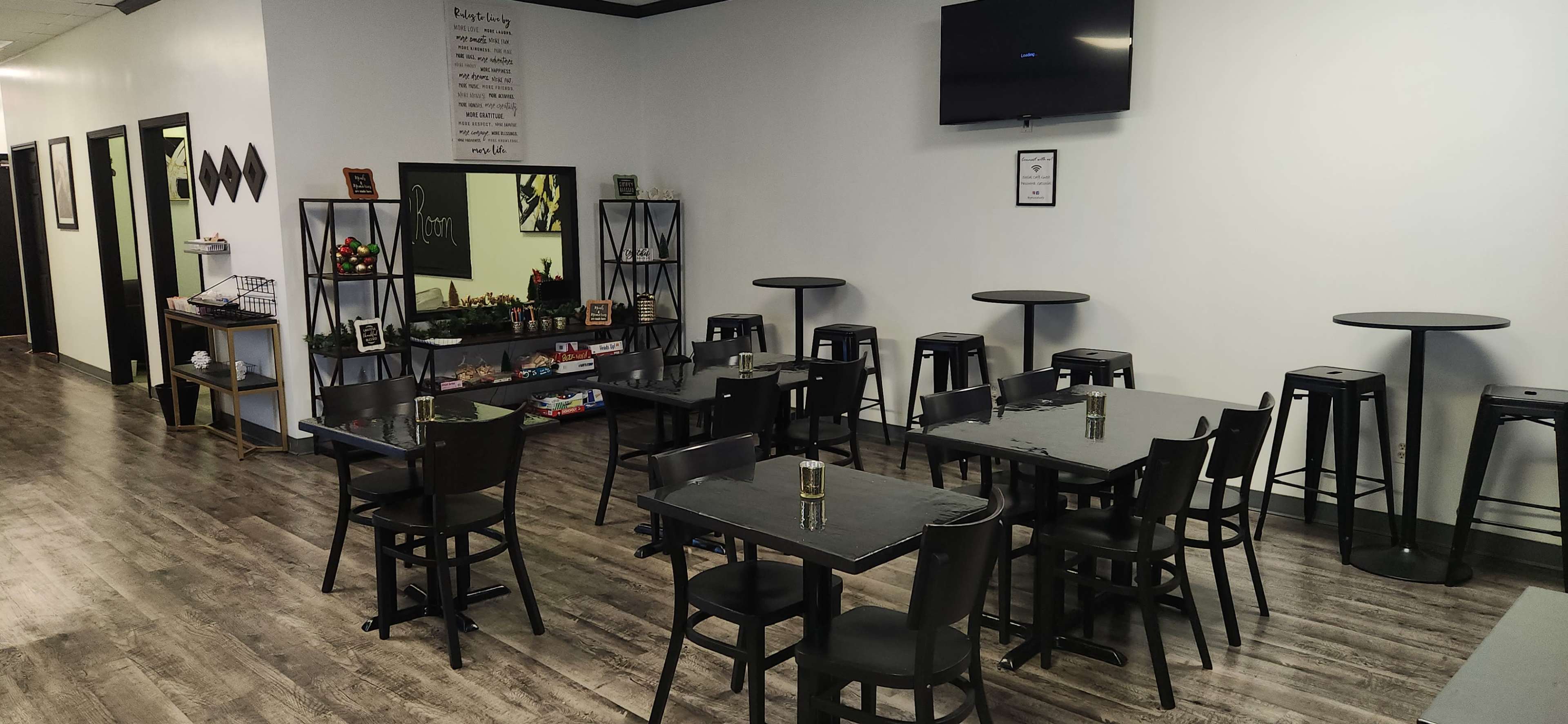 The image shows a dining area with several black tables and chairs, accompanied by tall bar stools and a wall-mounted television.