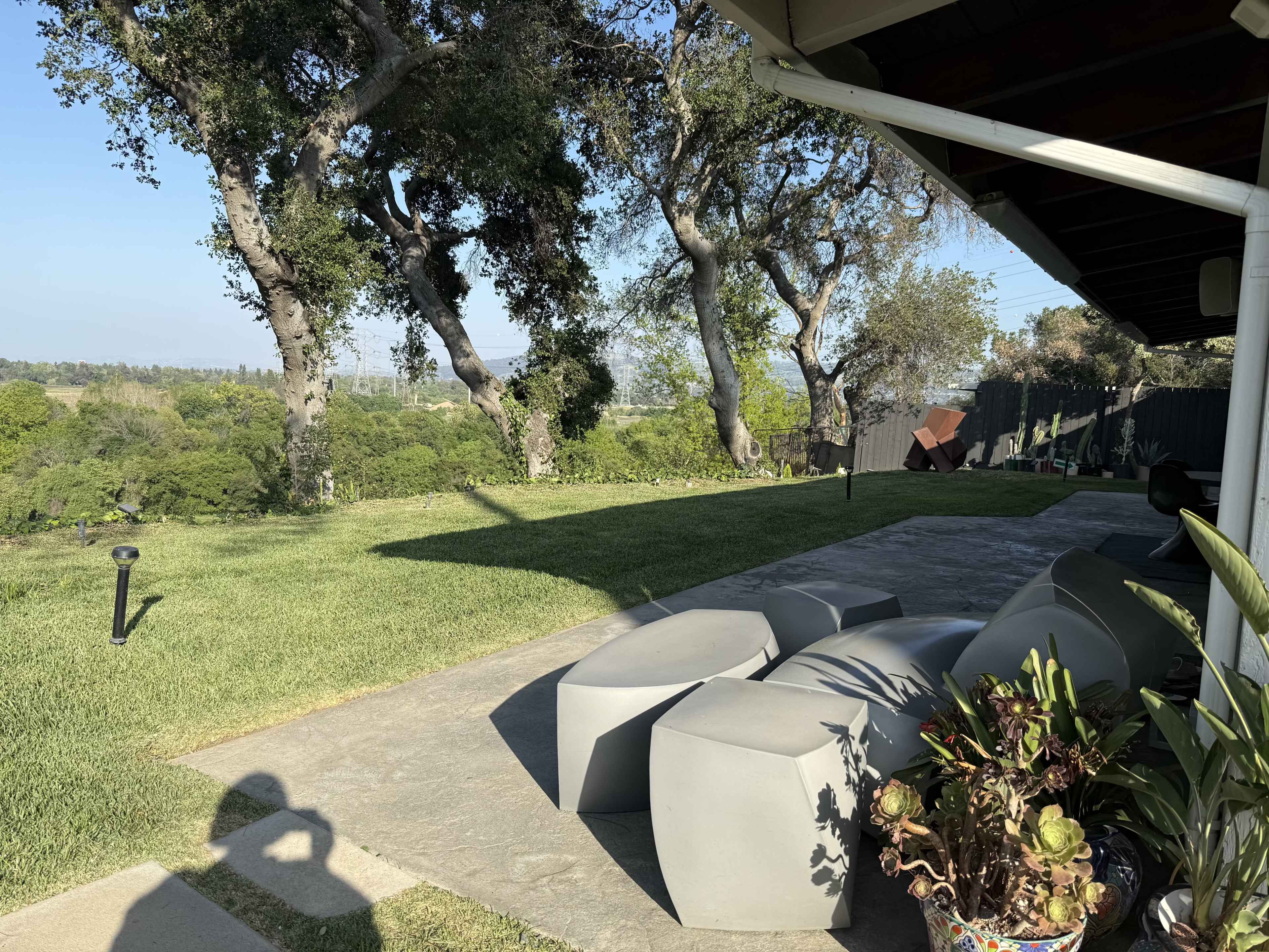 A patio area with modern seating overlooks a lush, green landscape and several trees under a clear blue sky.