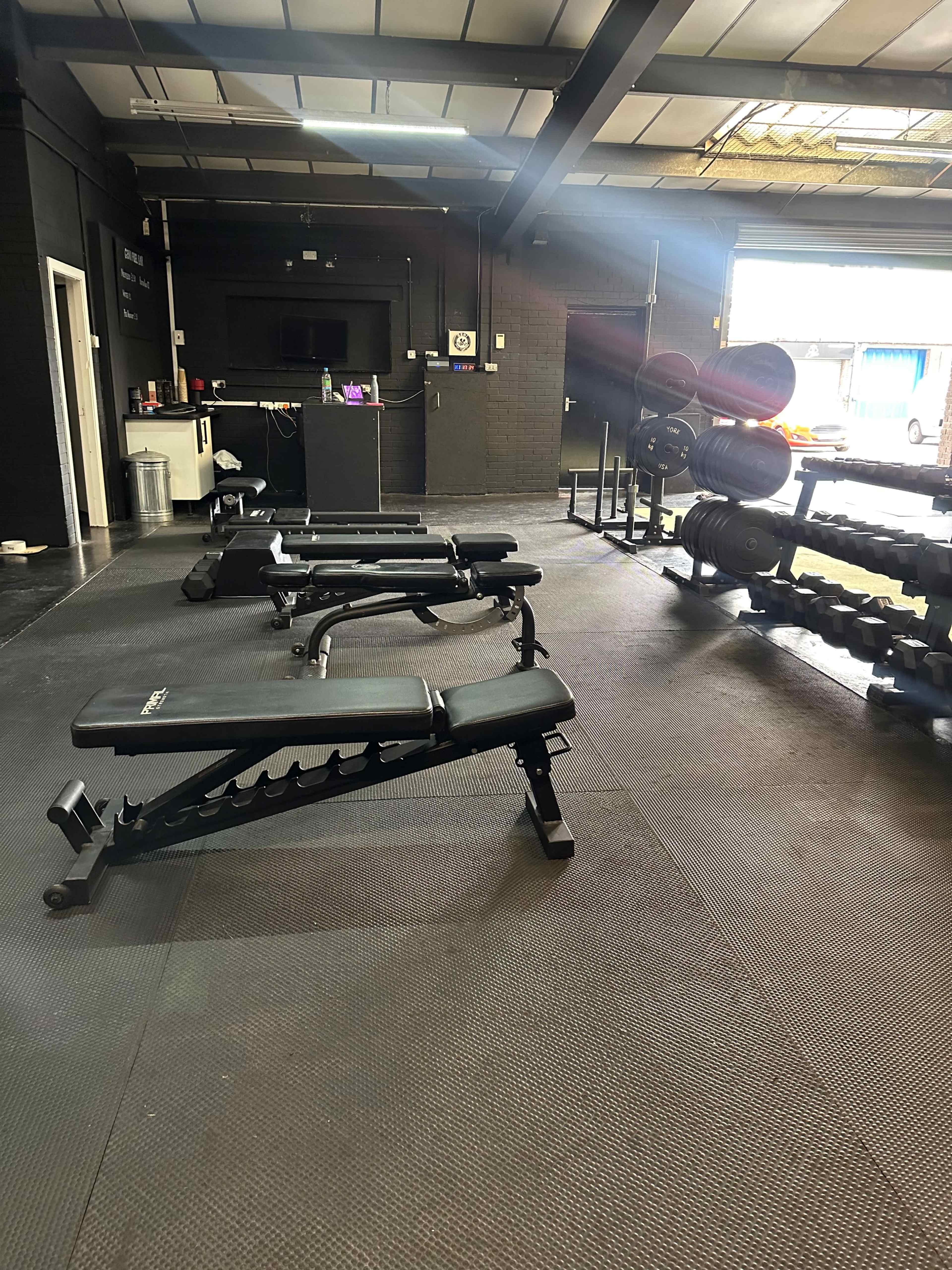 An empty gym with several adjustable benches and a rack of weights in the background.