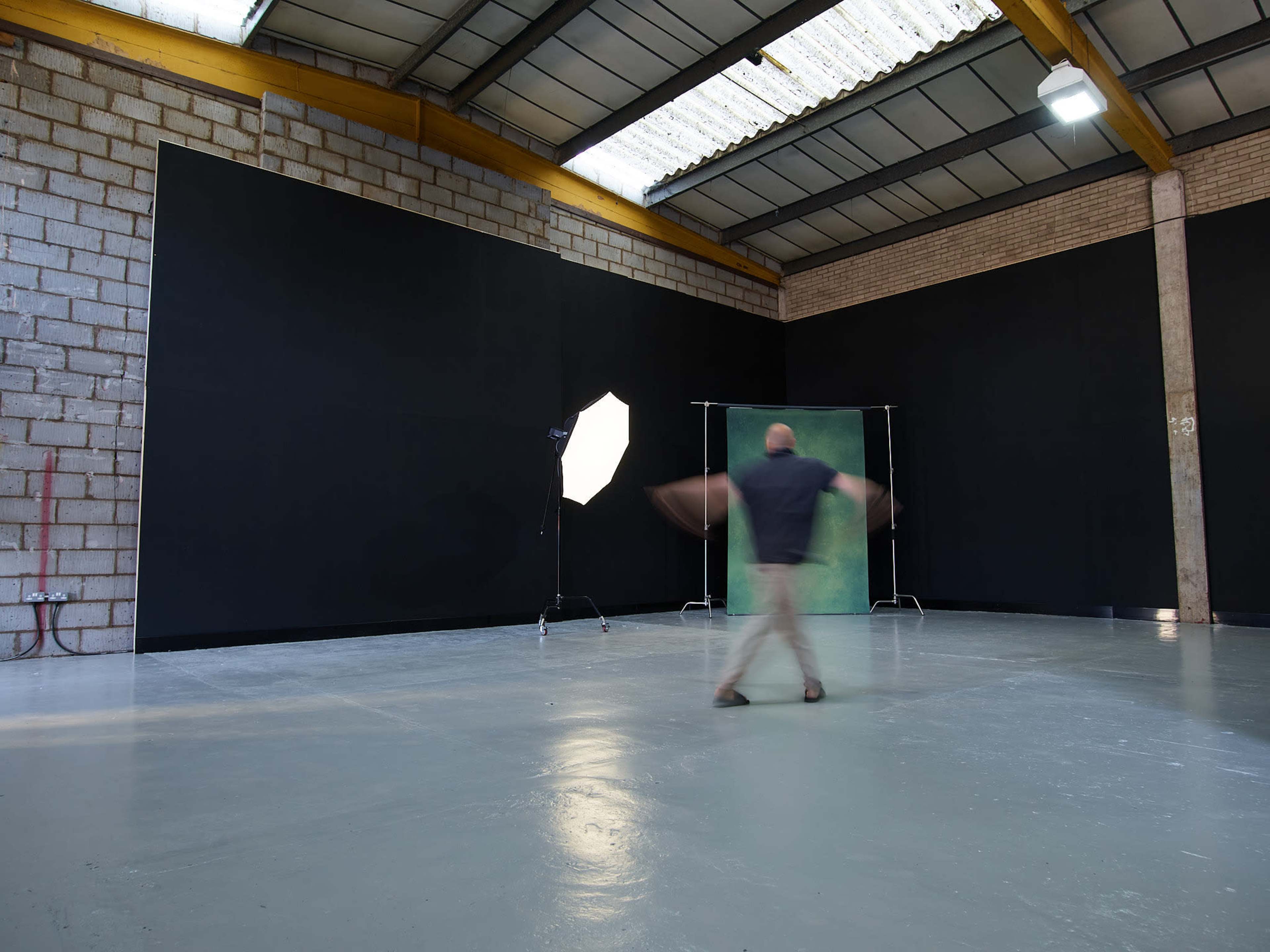 A person is captured mid-motion in an empty studio space with black walls and a backdrop, illuminated by a light source.