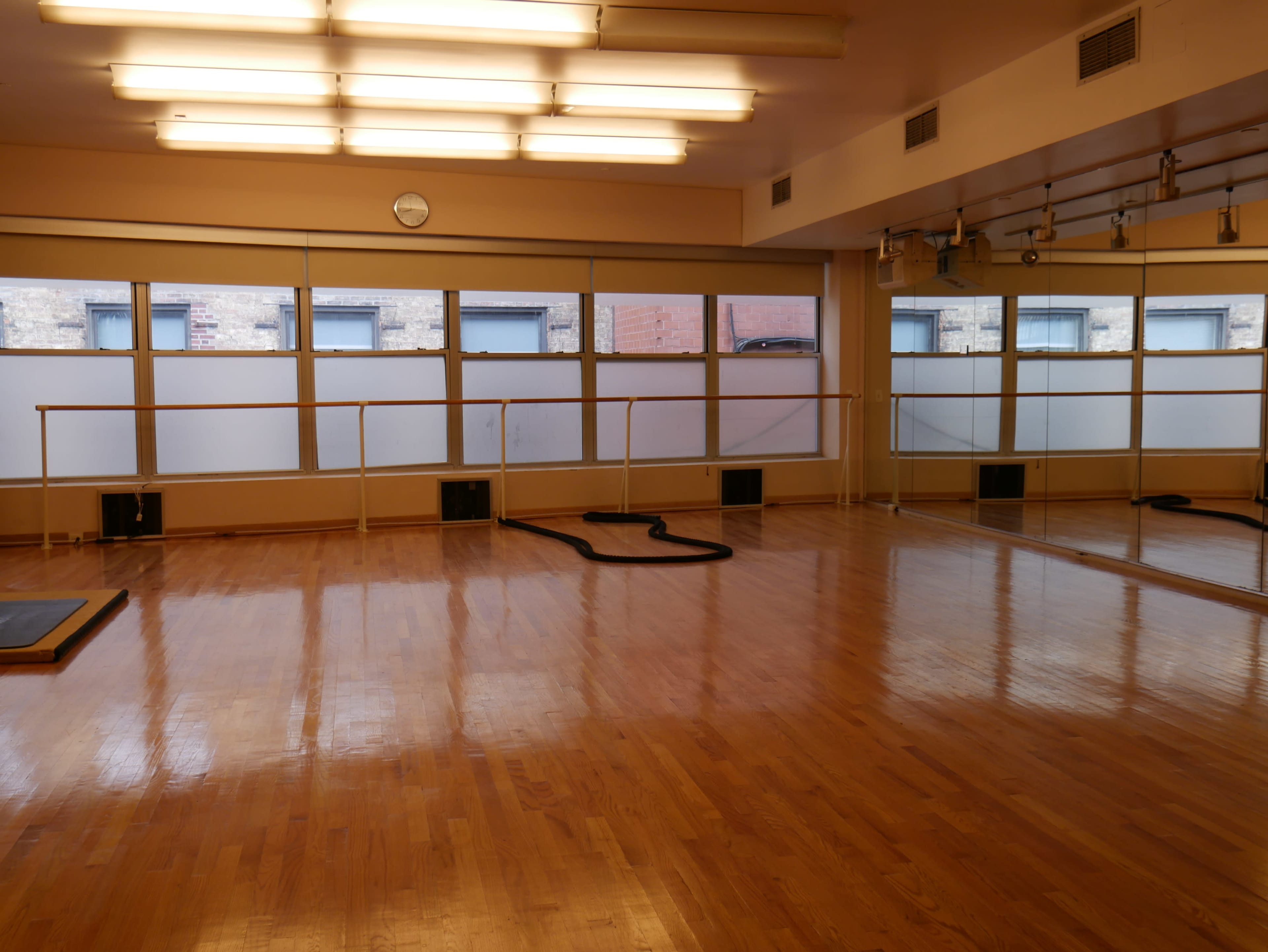 A spacious dance studio with wooden floors, large windows, and a ballet barre along one wall.