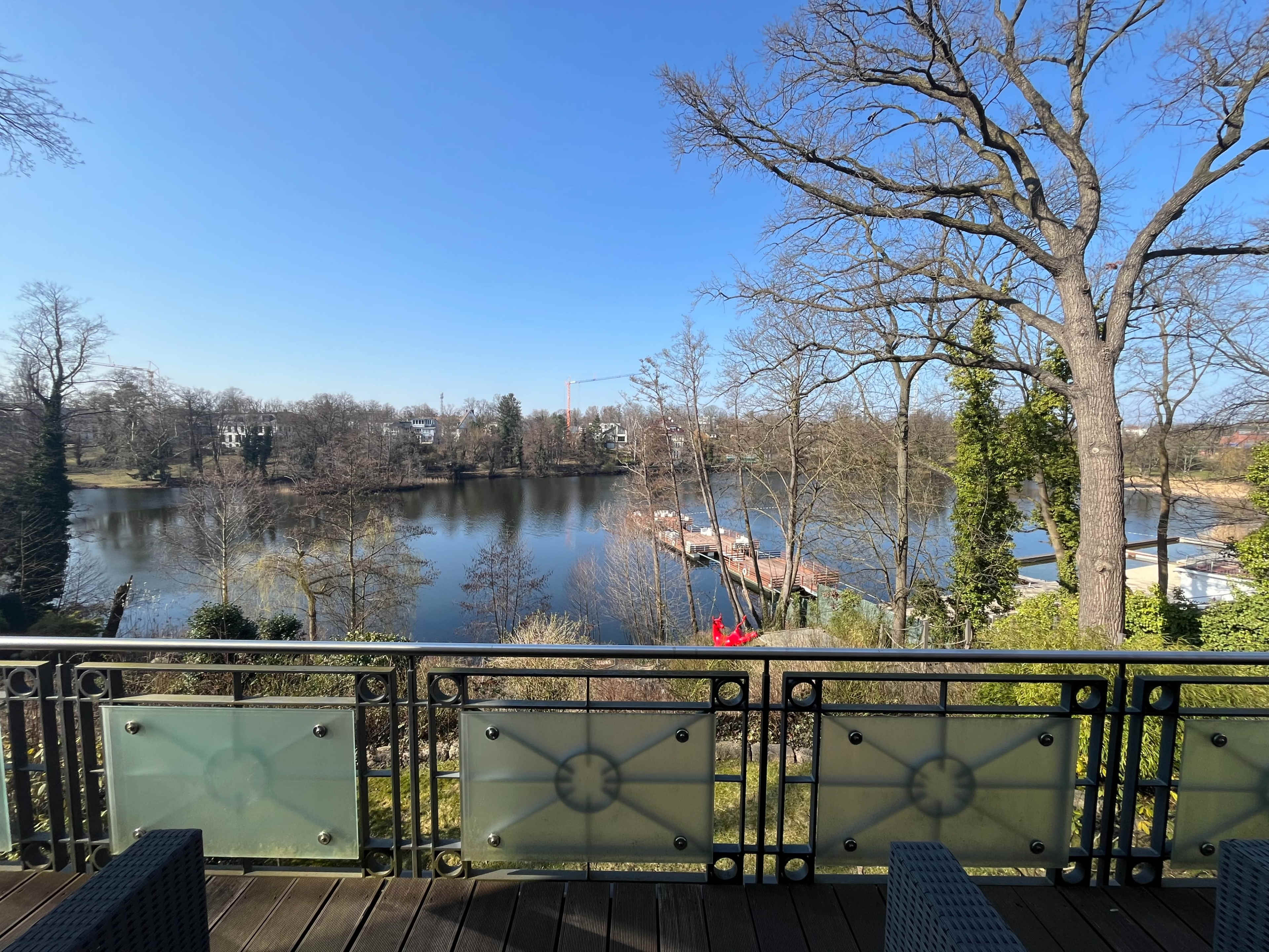 The image shows a scenic view of a lake surrounded by trees and a walkway, visible from a balcony with ornate railing.