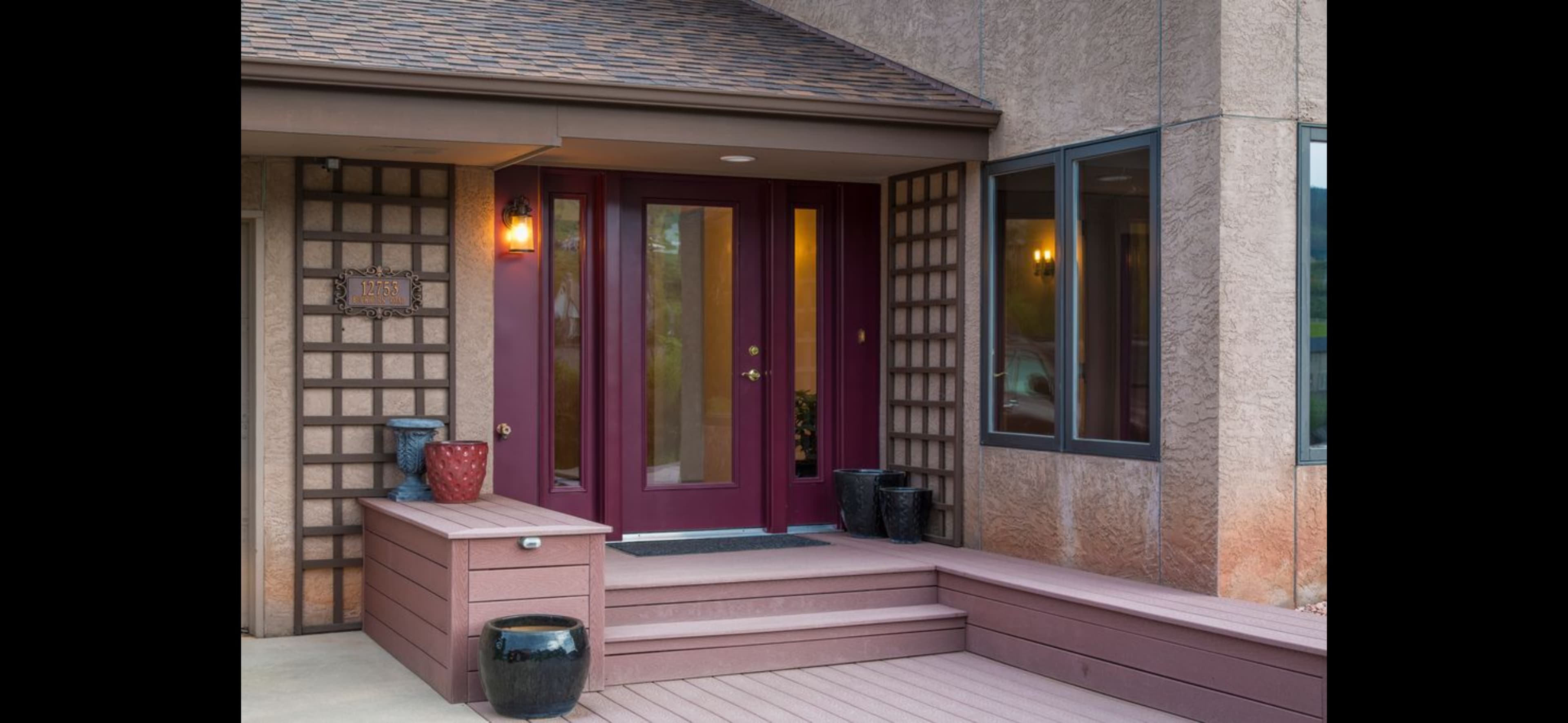 The image shows a modern house entrance with two red doors, a small set of stairs, and decorative vases placed on the porch.