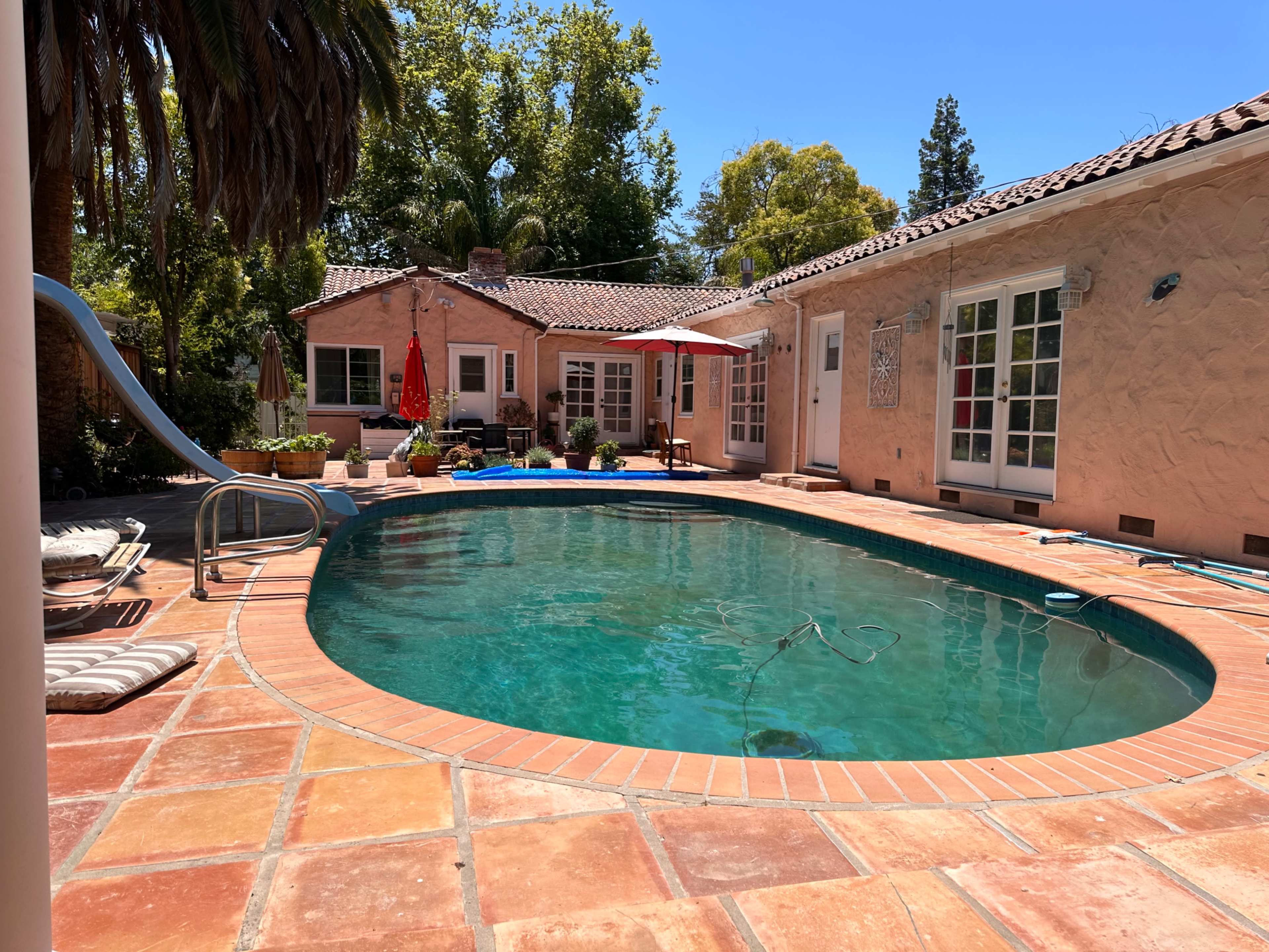 The image shows a private pool surrounded by a patio and a house with a tile roof and sliding glass doors.