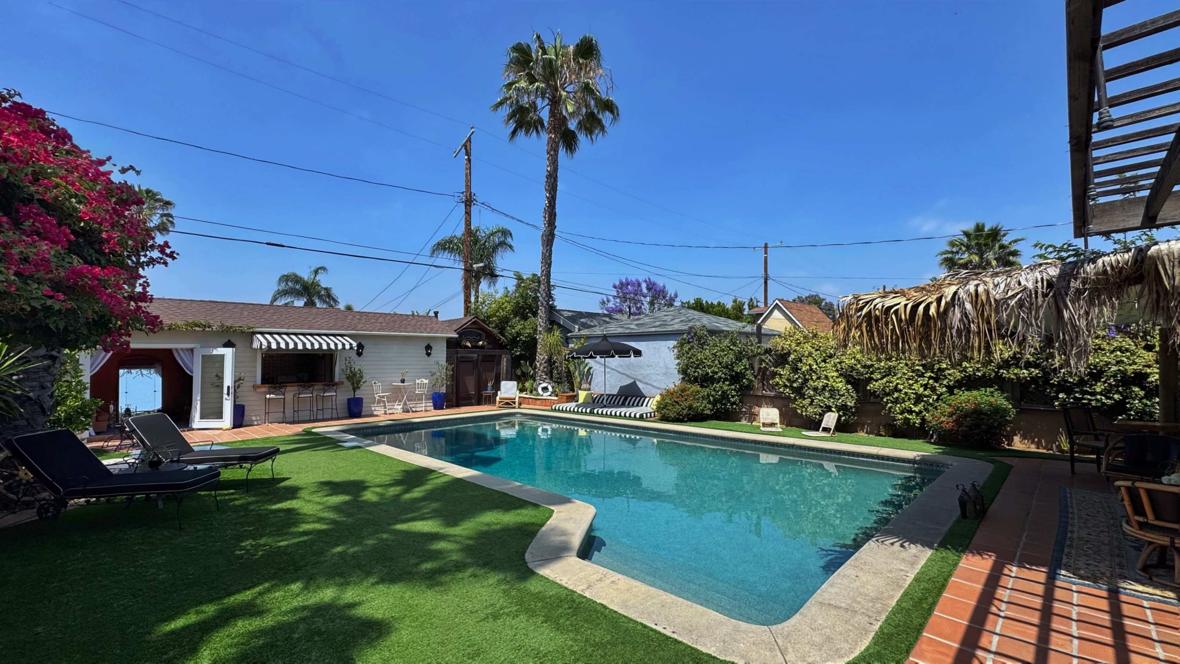 The image shows a swimming pool surrounded by palm trees and lush greenery in a residential backyard.