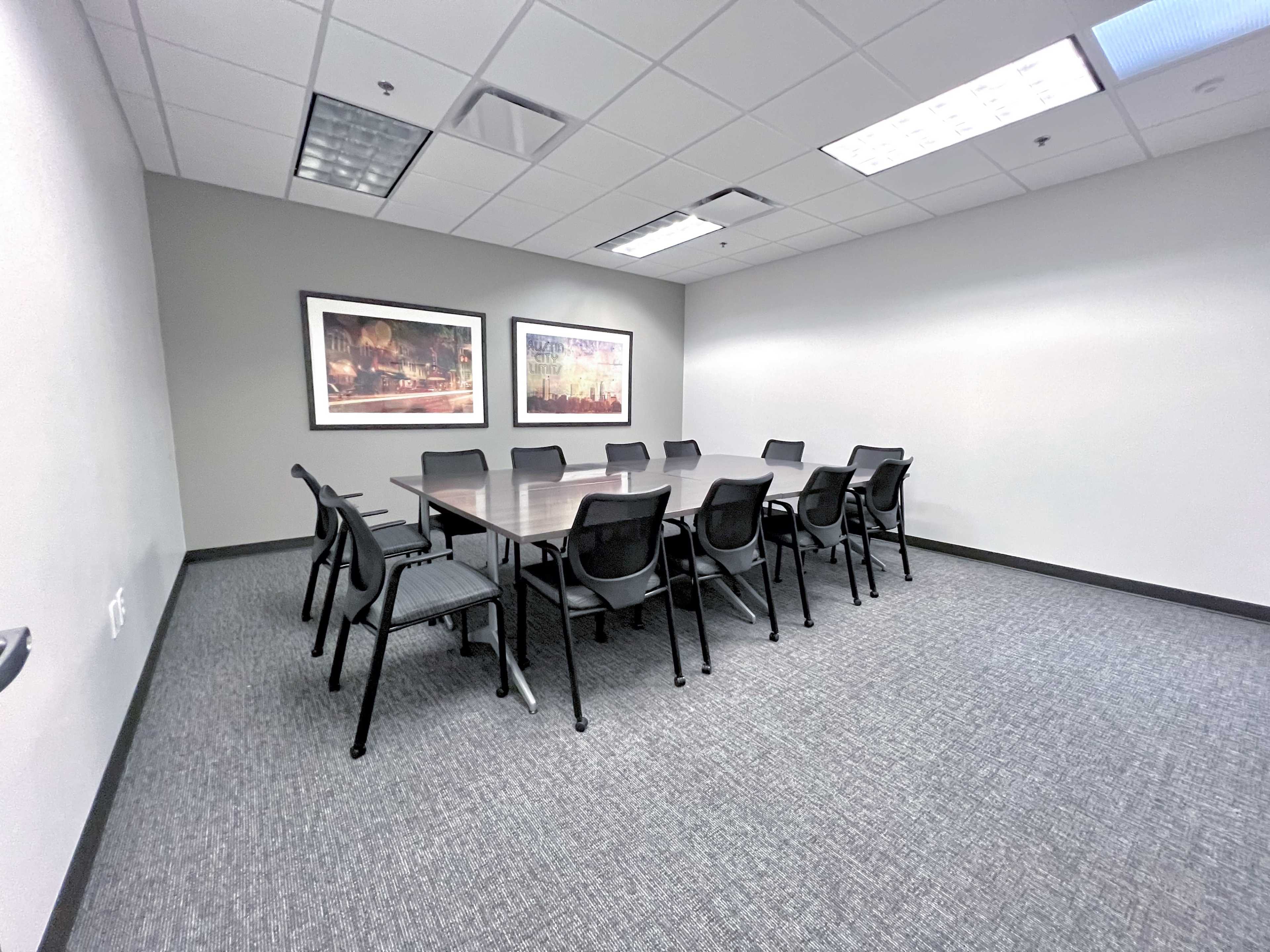 A large conference room with a rectangular table surrounded by twelve chairs and two framed artworks on the walls.