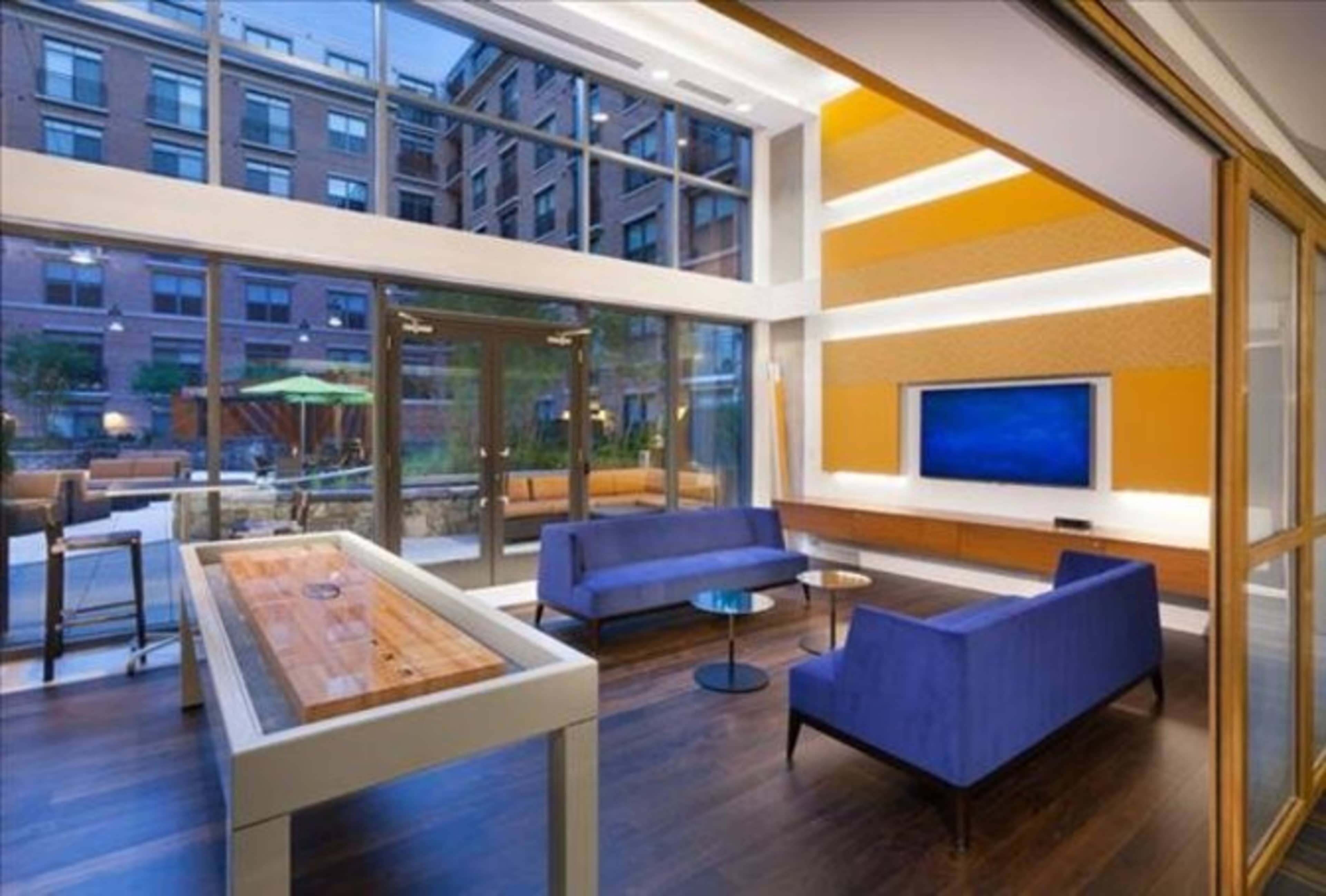 A modern lounge area with blue sofas, a coffee table, and a large window overlooking an outdoor space.