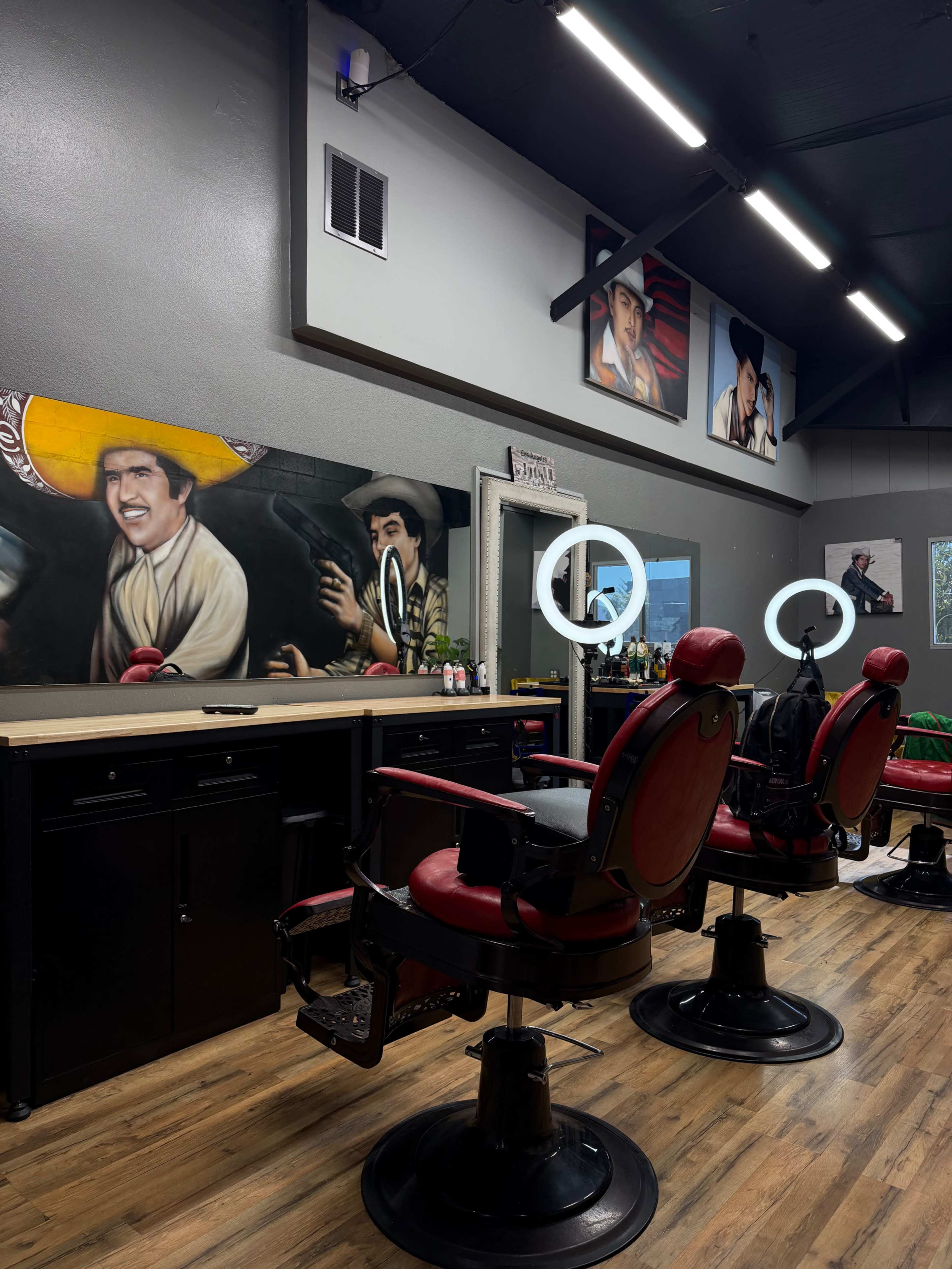 The image shows a barbershop interior with two red barber chairs, a long counter with mirrors, and paintings of men on the walls.