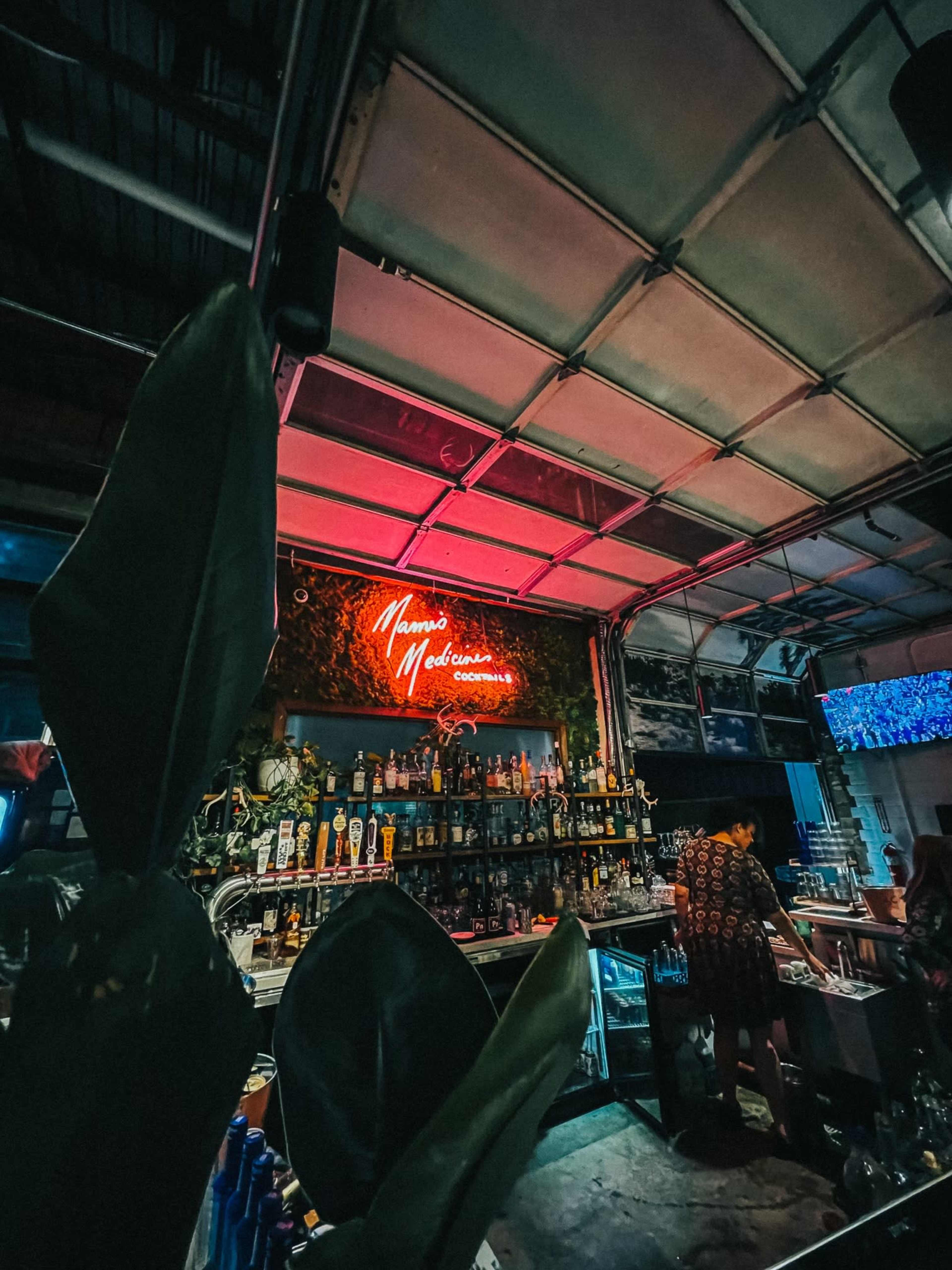 A bar interior features a neon sign reading "Mamma's Medusas" with shelves stocked with various bottles in the background.