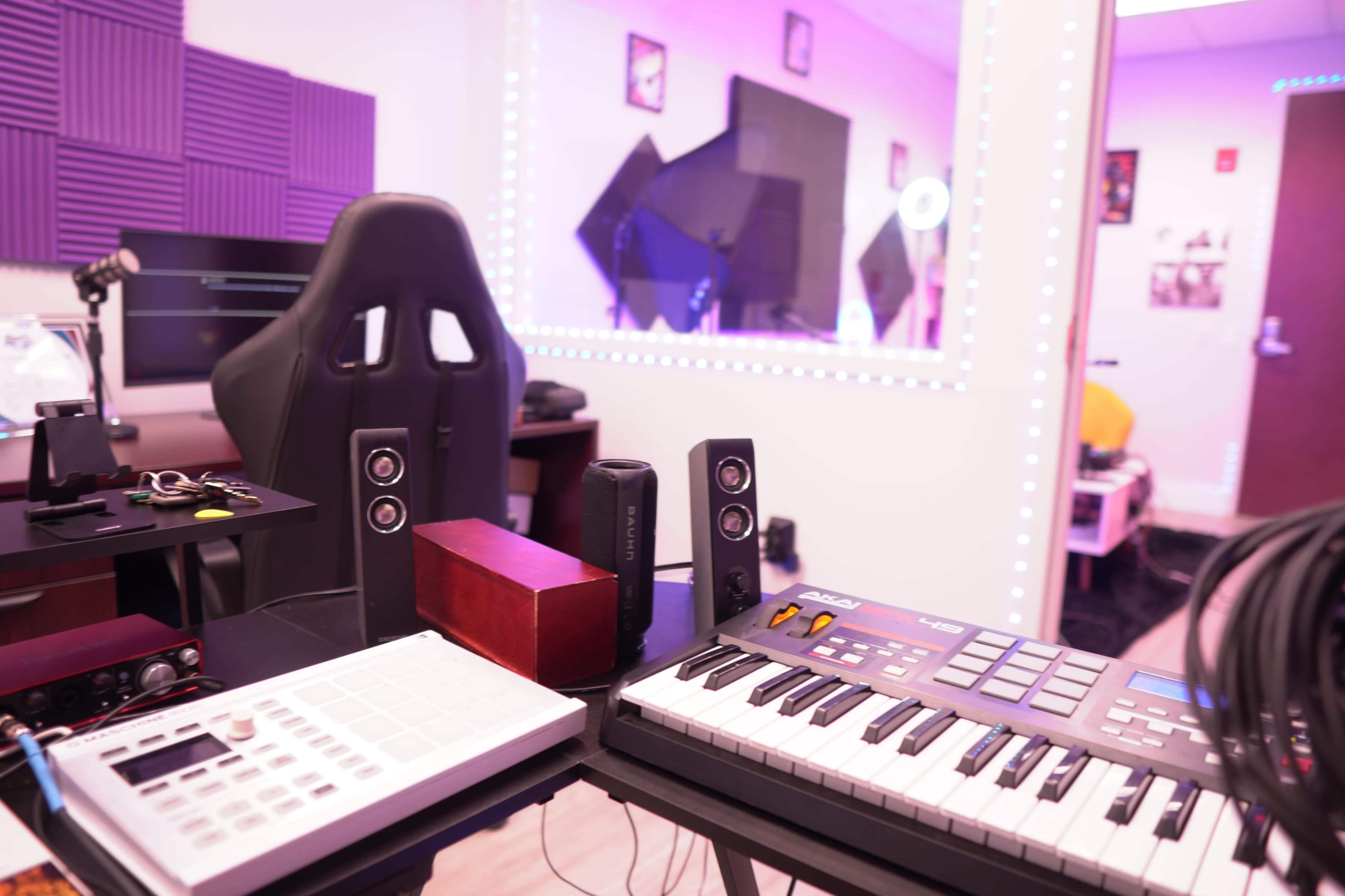 A music production setup with a keyboard, a sound mixer, speakers, and a purple-lit background.