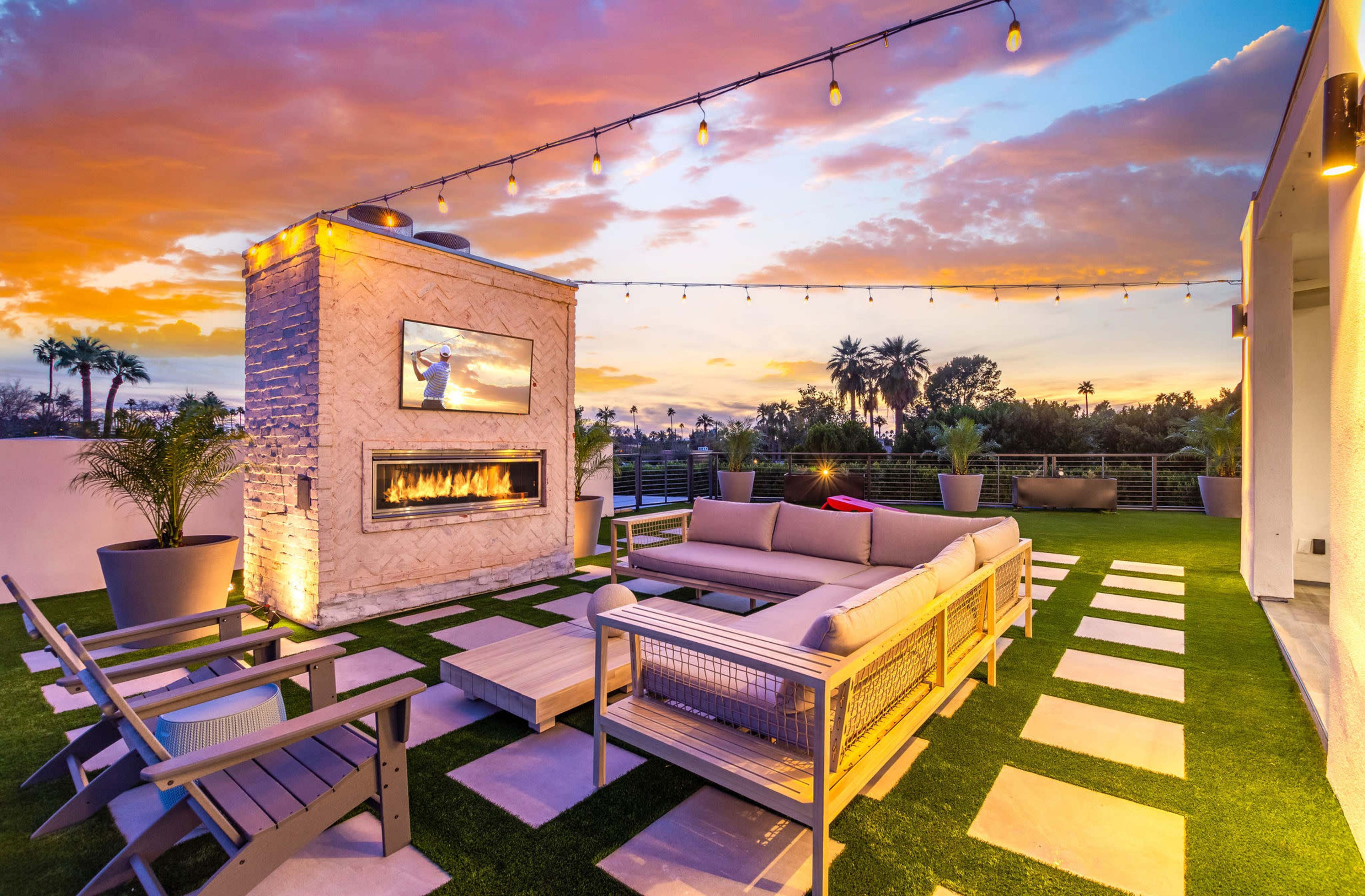 A modern rooftop terrace with a fire pit, a large sofa, and decorative lighting against a vibrant sunset sky.